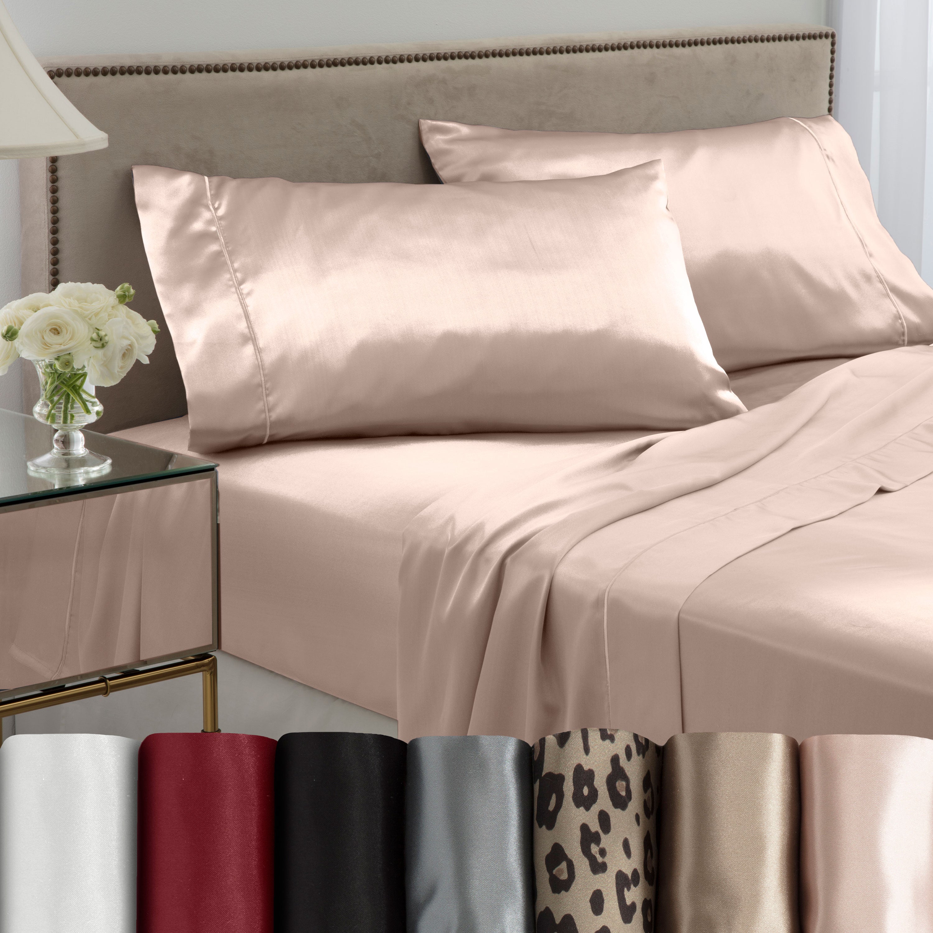 Satin sheet set in various colors displayed on a bed with matching pillows and a bedside table with flowers.