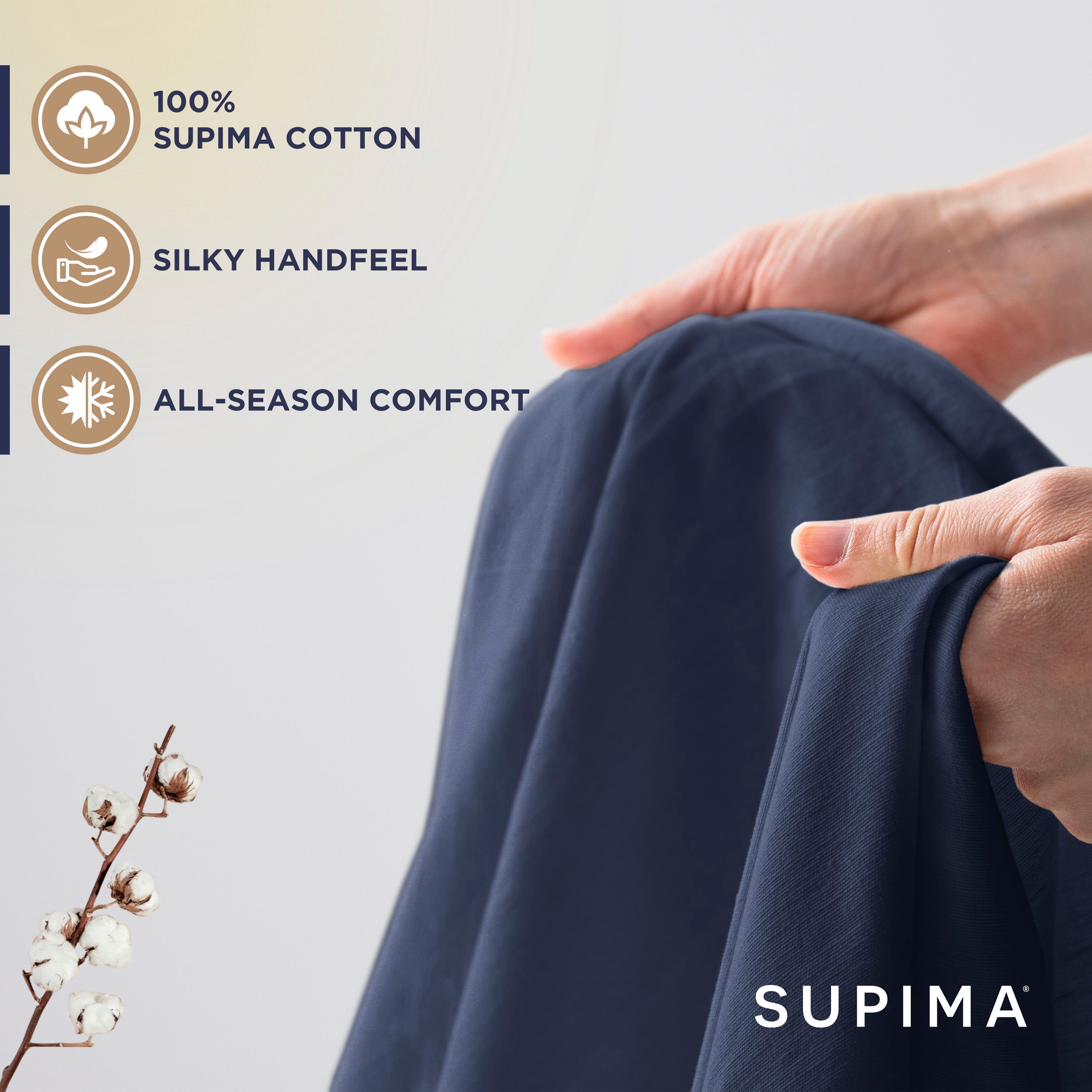 Hands holding a dark blue sheet, showcasing its soft texture, with a cotton plant branch in the foreground.