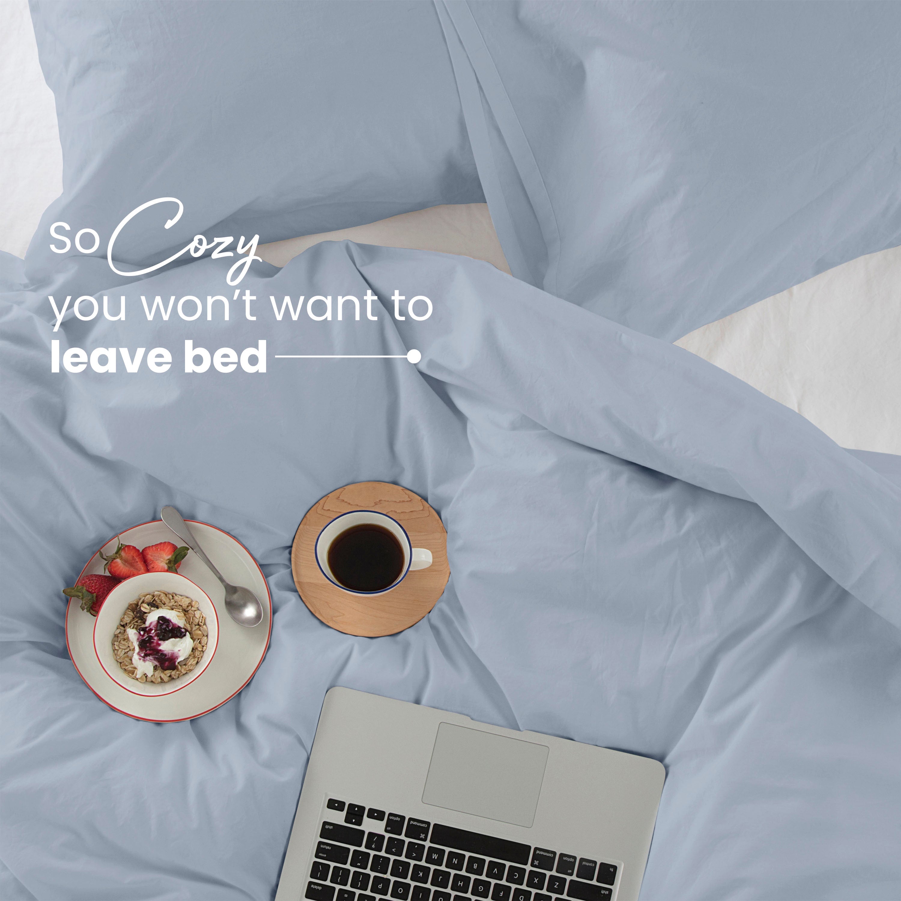 Cozy bedroom scene with light blue comforter set, laptop, and breakfast on a wooden coaster.