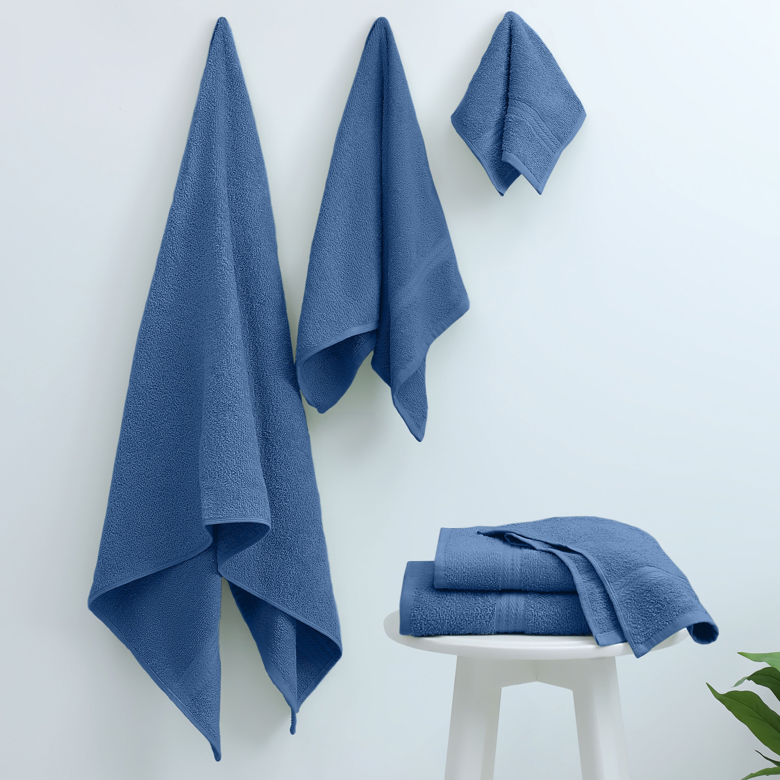 Three blue towels hanging on a wall and two folded towels on a white stool.