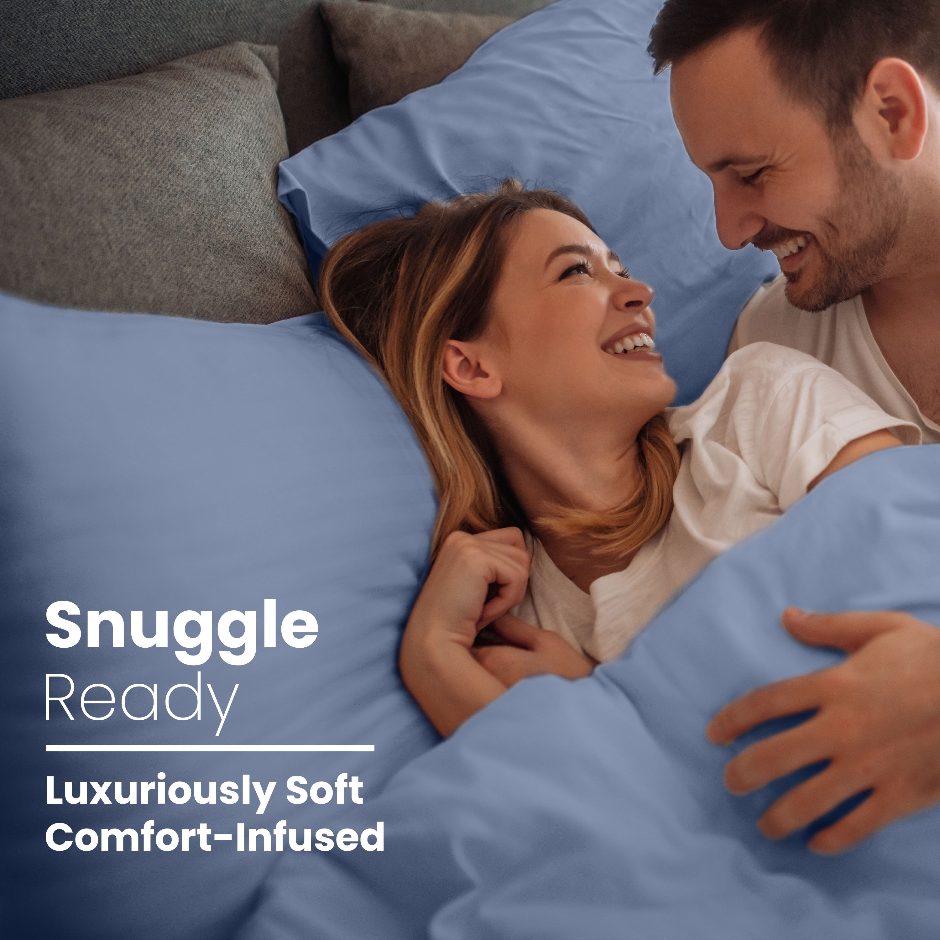 Couple smiling and cuddling in bed with blue cotton sheets and pillows.