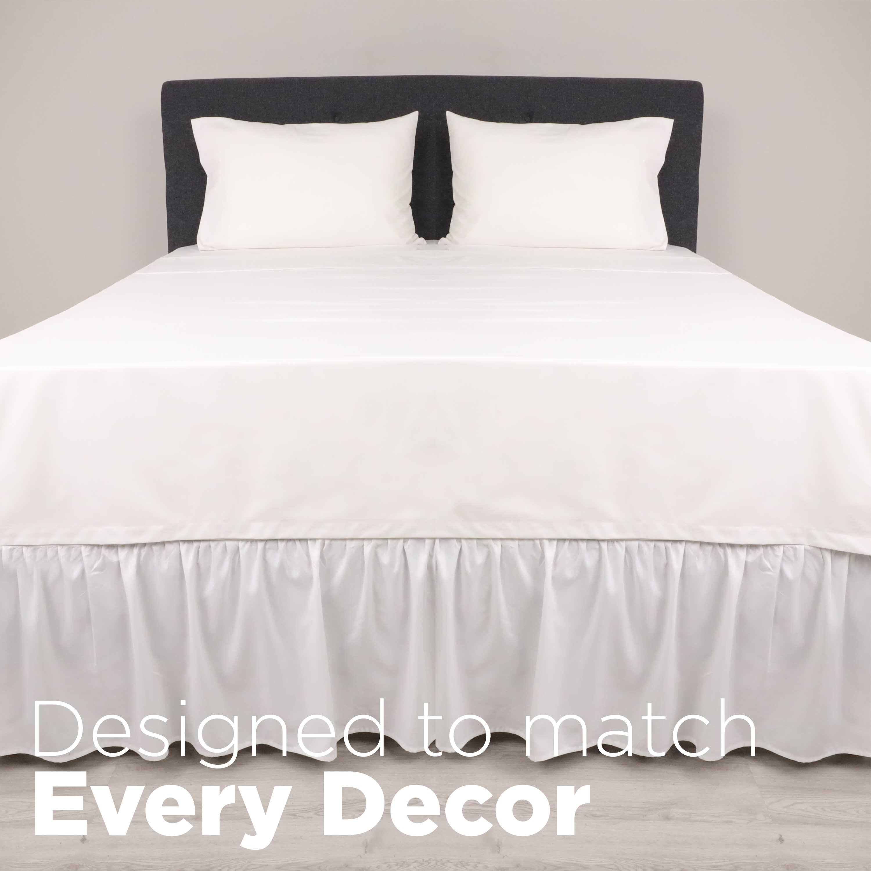 White ruffle bed skirt drapes over the edge of a bed with two white pillows on a gray headboard.