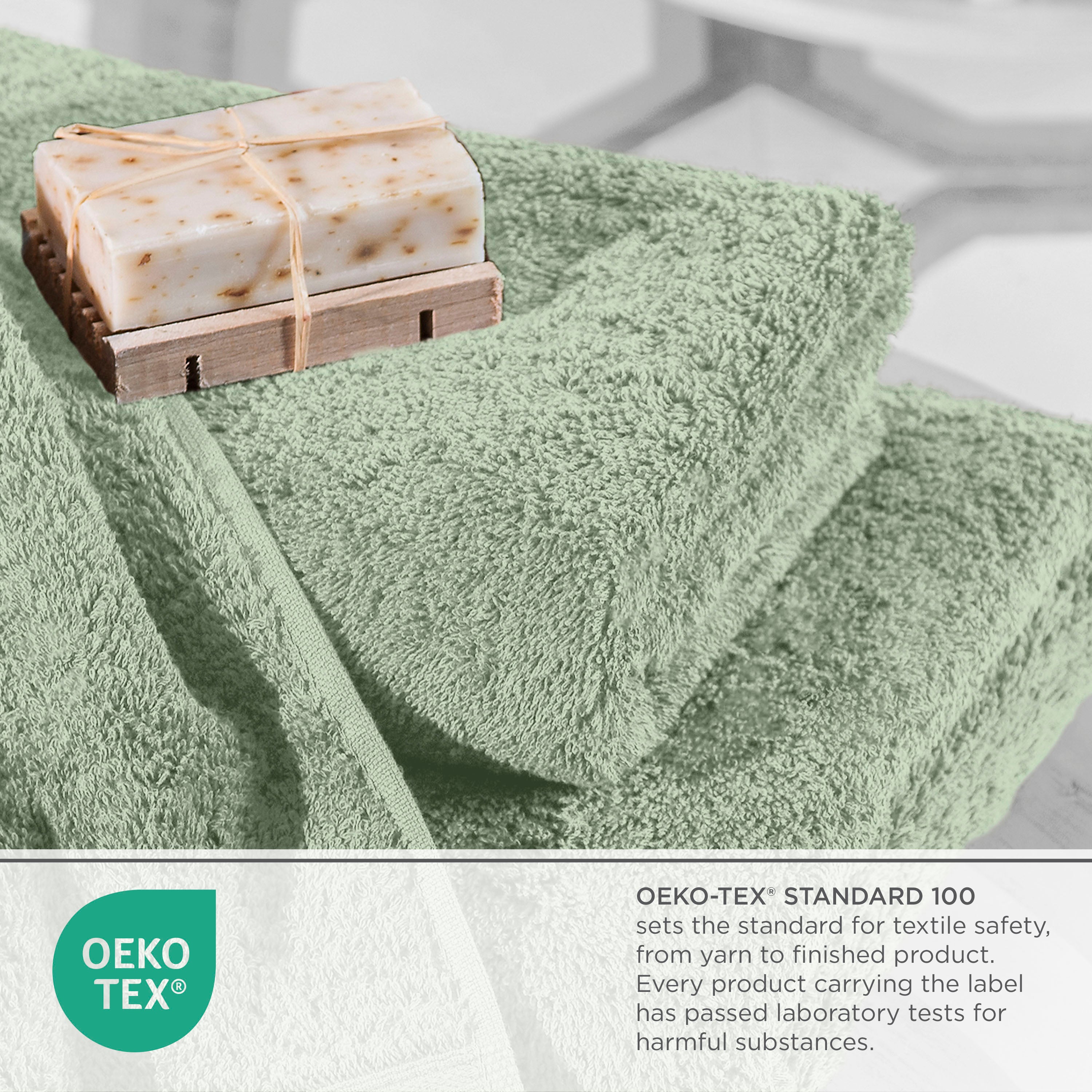 Soft green towels stacked with a bar of soap on a wooden soap dish, featuring Oeko-Tex certification label.
