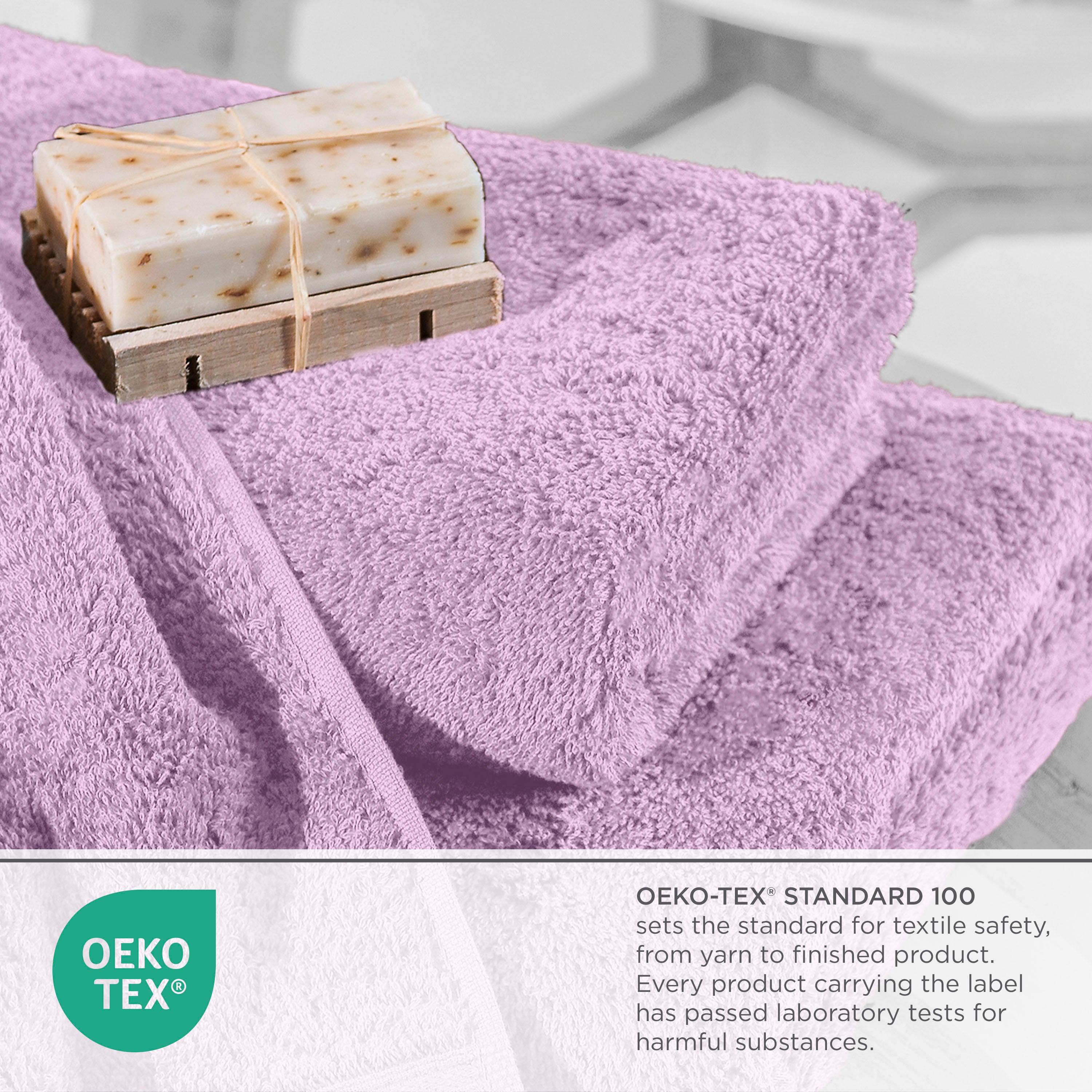 Lavender towels stacked with a bar of soap on a wooden soap dish, featuring Oeko-Tex certification label.