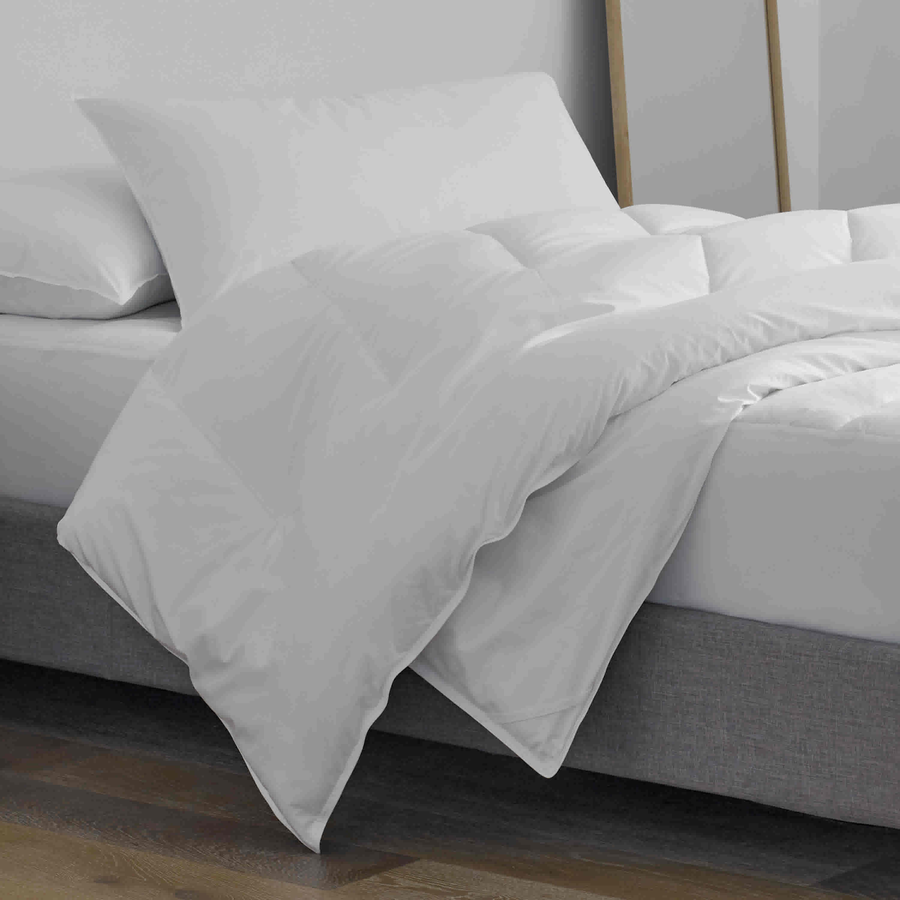 White pillow and pillow protector set placed on a bed with a gray base and wooden floor.