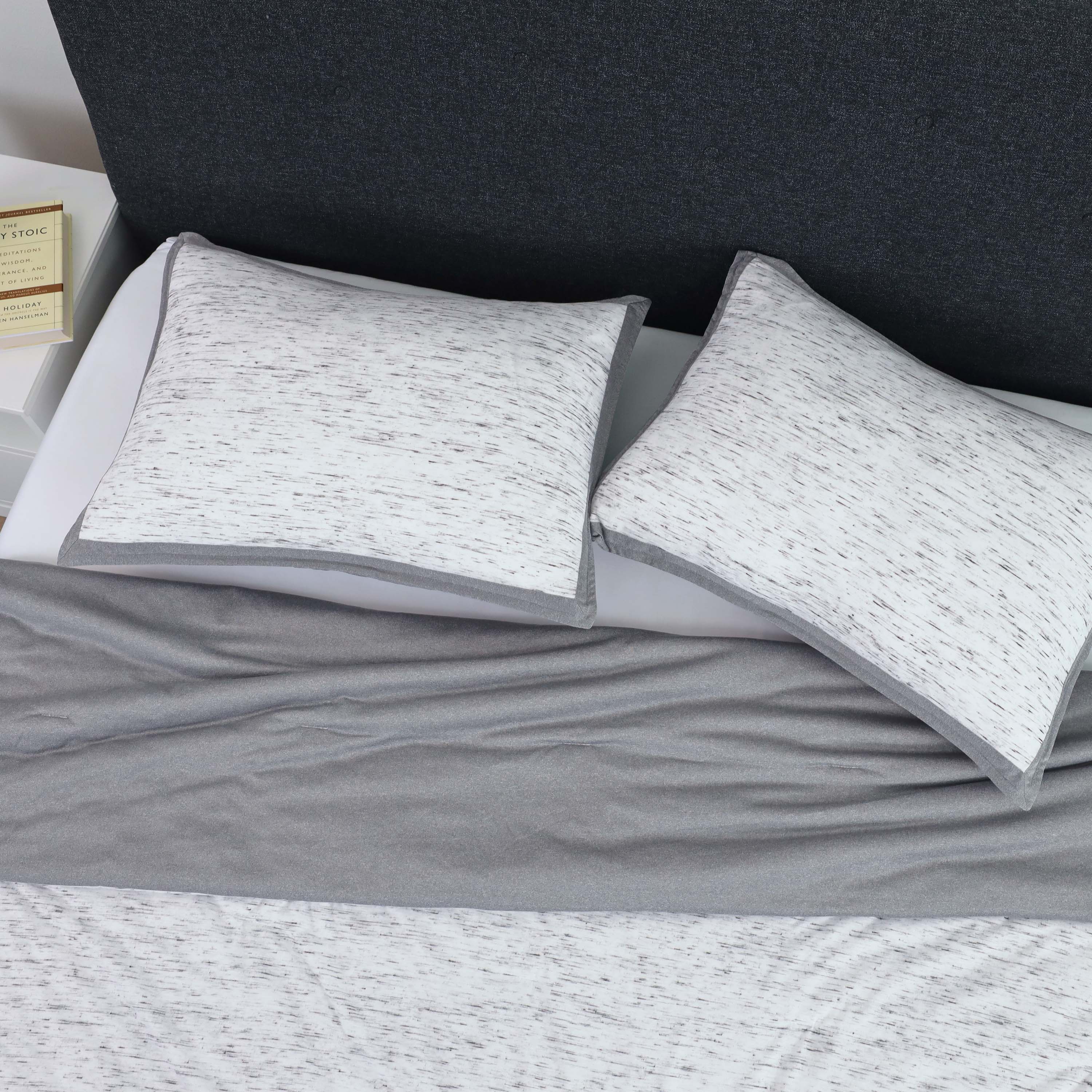 Gray and white patterned pillows on a bed with a gray blanket and a dark headboard in the background.