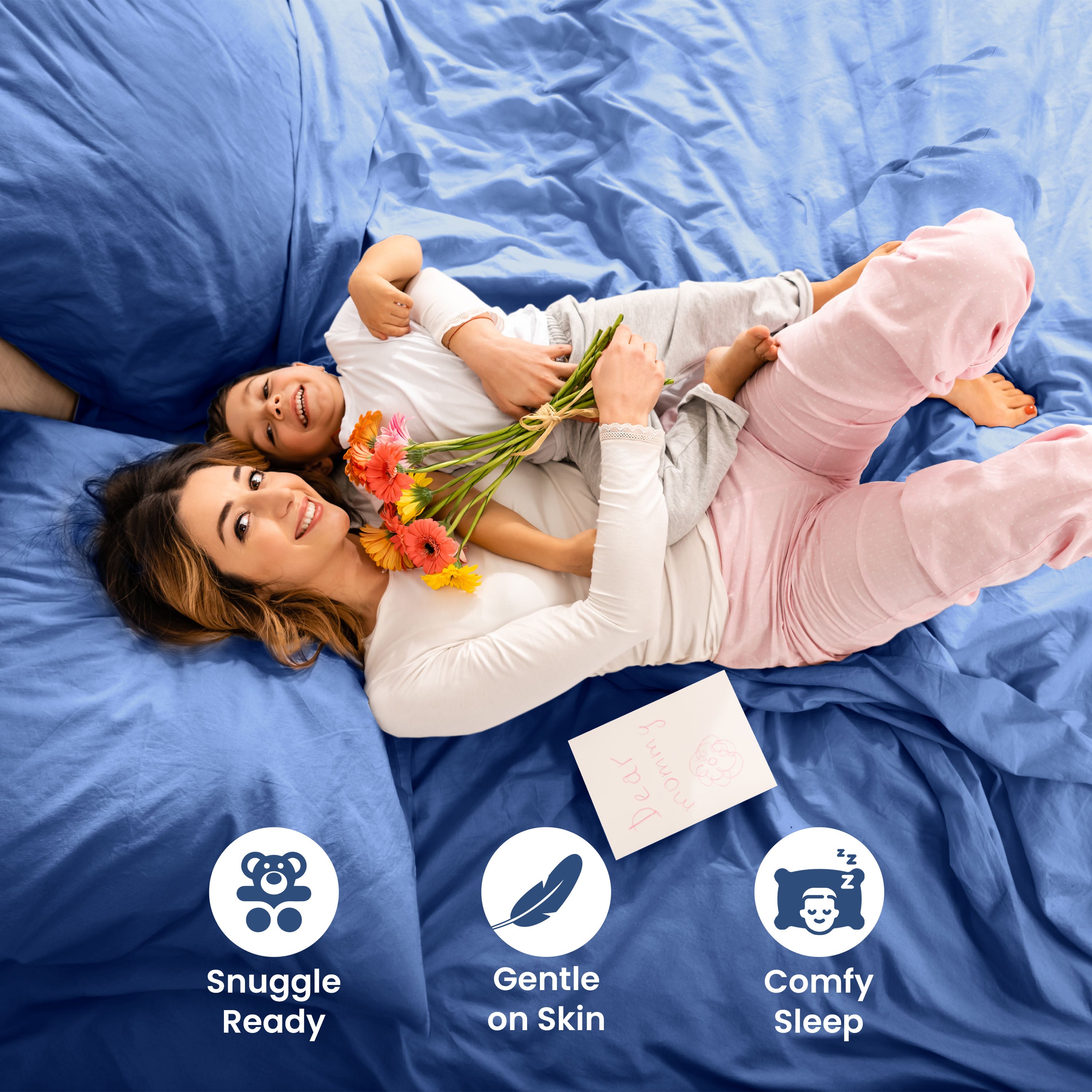 A woman and child are lying on a blue bed, with the woman holding flowers and a card.
