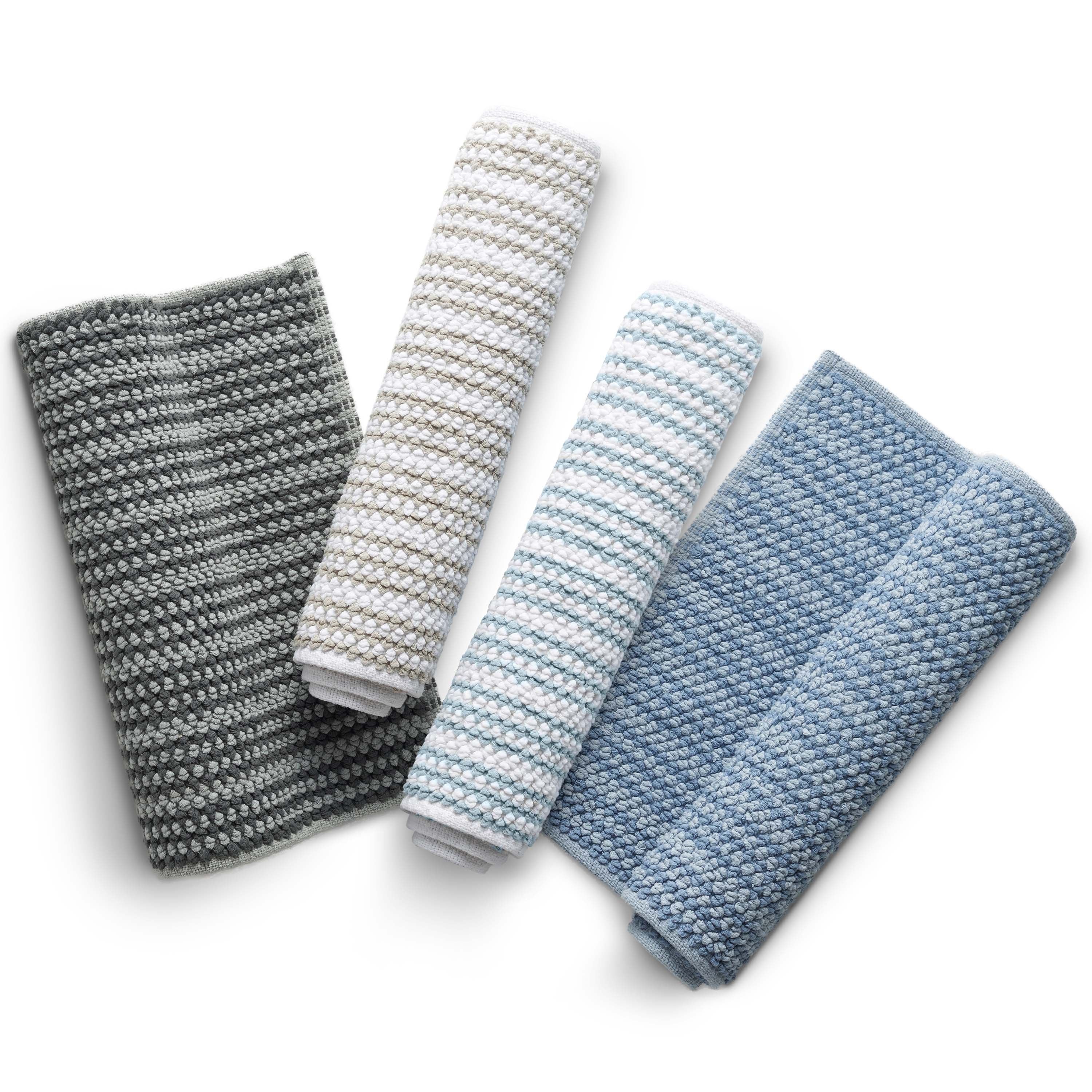 Four rolled bath rugs in varying shades of gray, white, and blue with a textured stripe pattern.