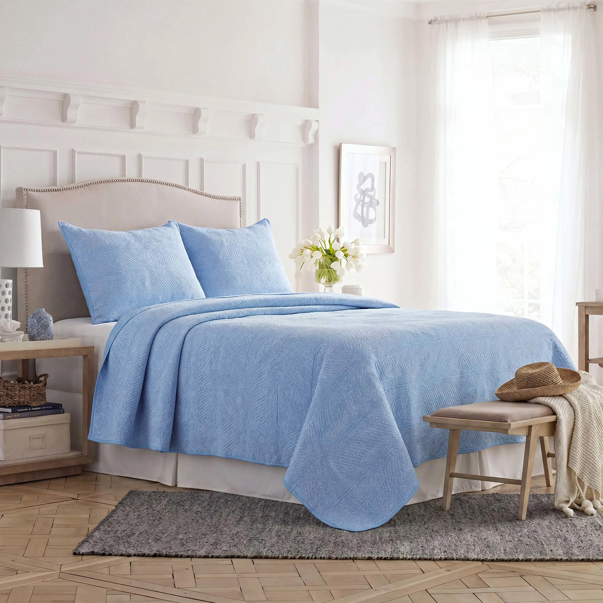 Side view of blue Southern Tide quilt and shams on a bed.