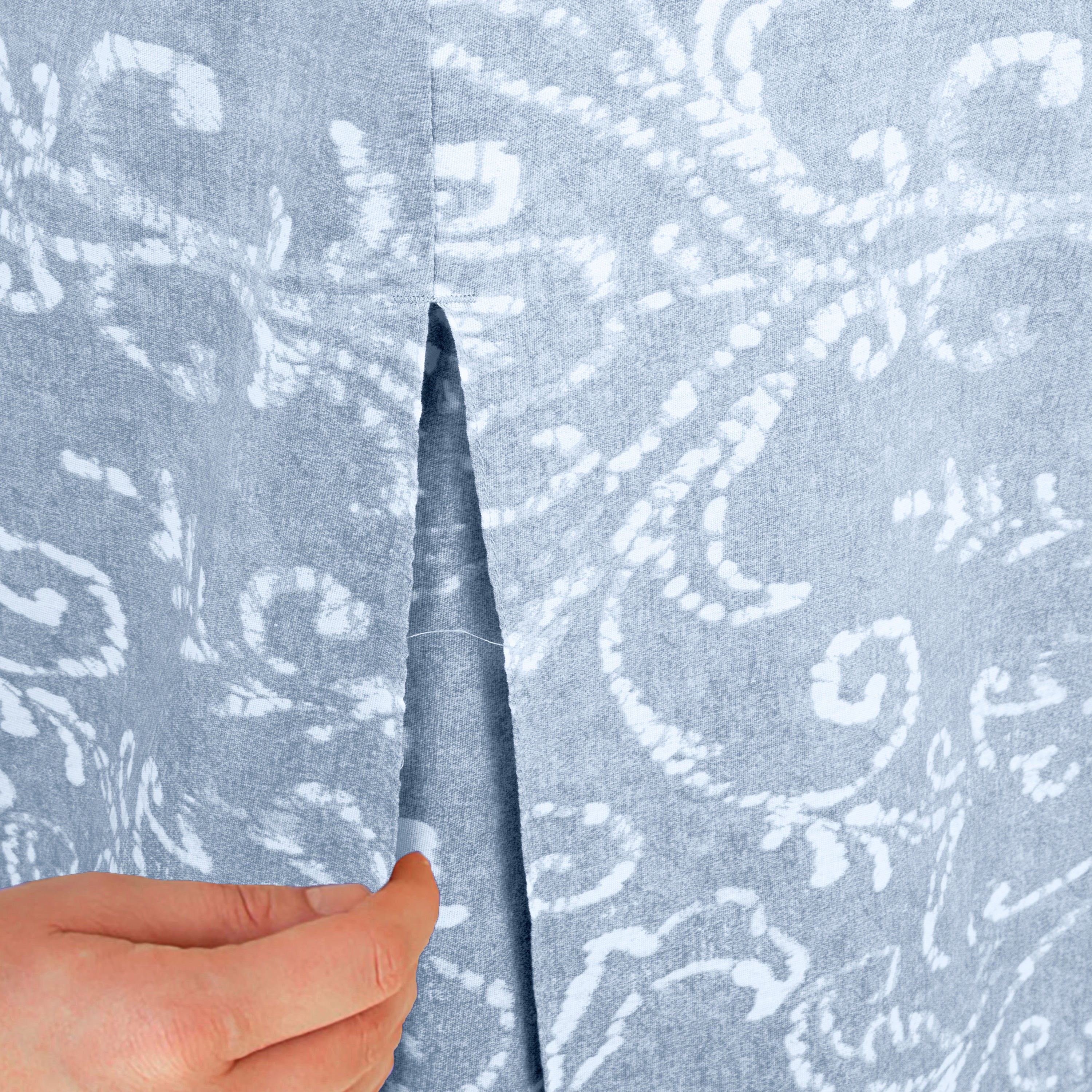 Close-up of a hand holding a slit in a light blue table cover with a white paisley pattern.