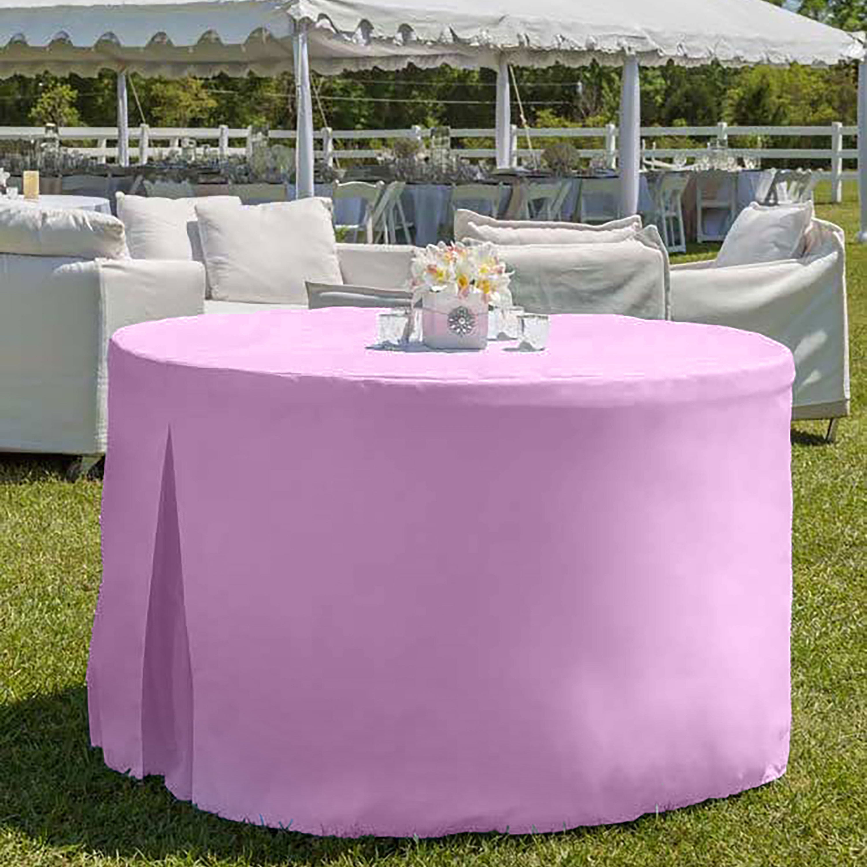 Round table covered with a pink tablecloth, set outdoors with a floral centerpiece and chairs in the background.