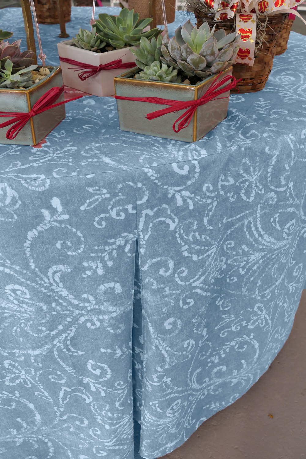 Round table covered with a light blue patterned tablecloth, featuring small potted succulents on top.