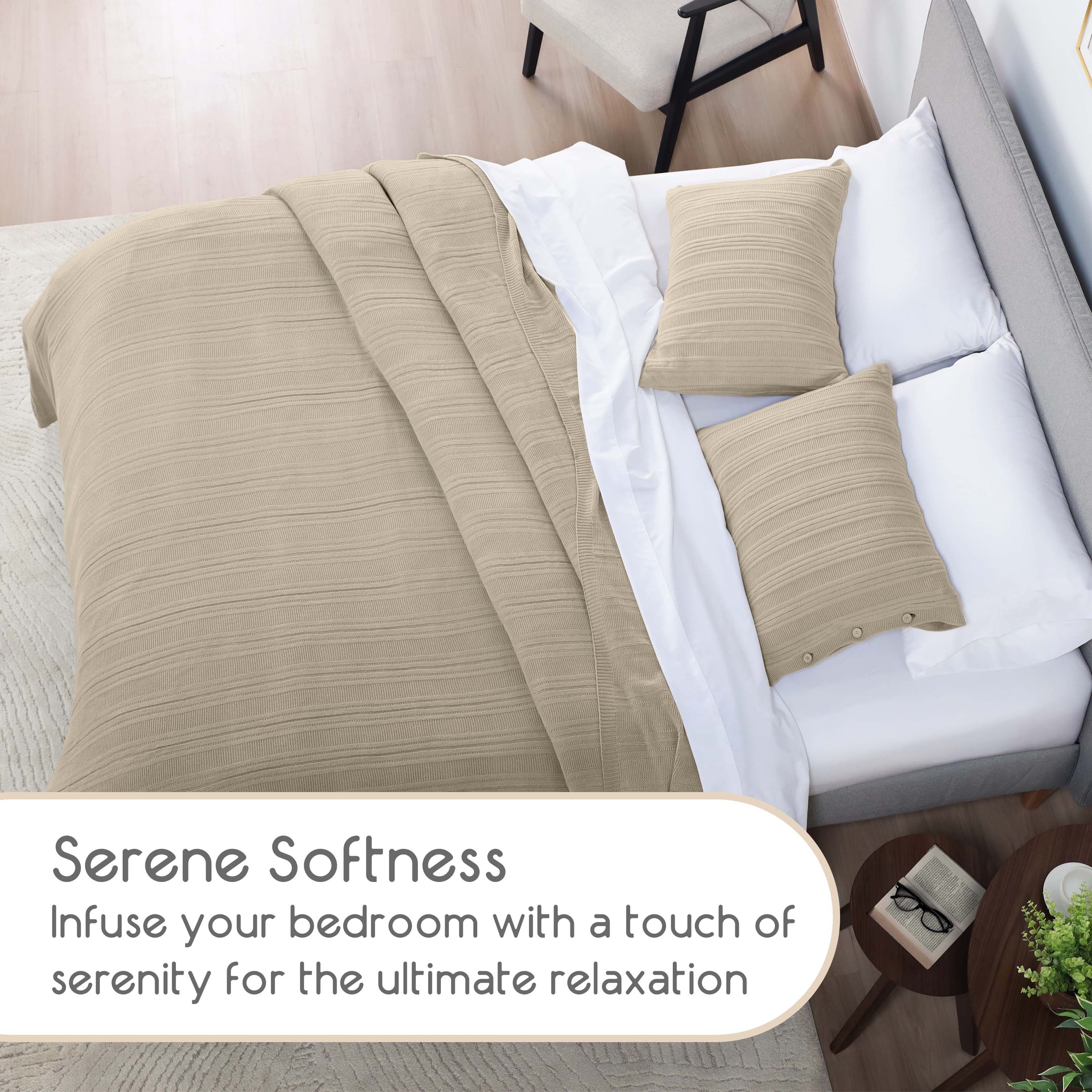 Beige blanket set draped over a bed with two matching pillows on white bedding, beside a small table and chair.