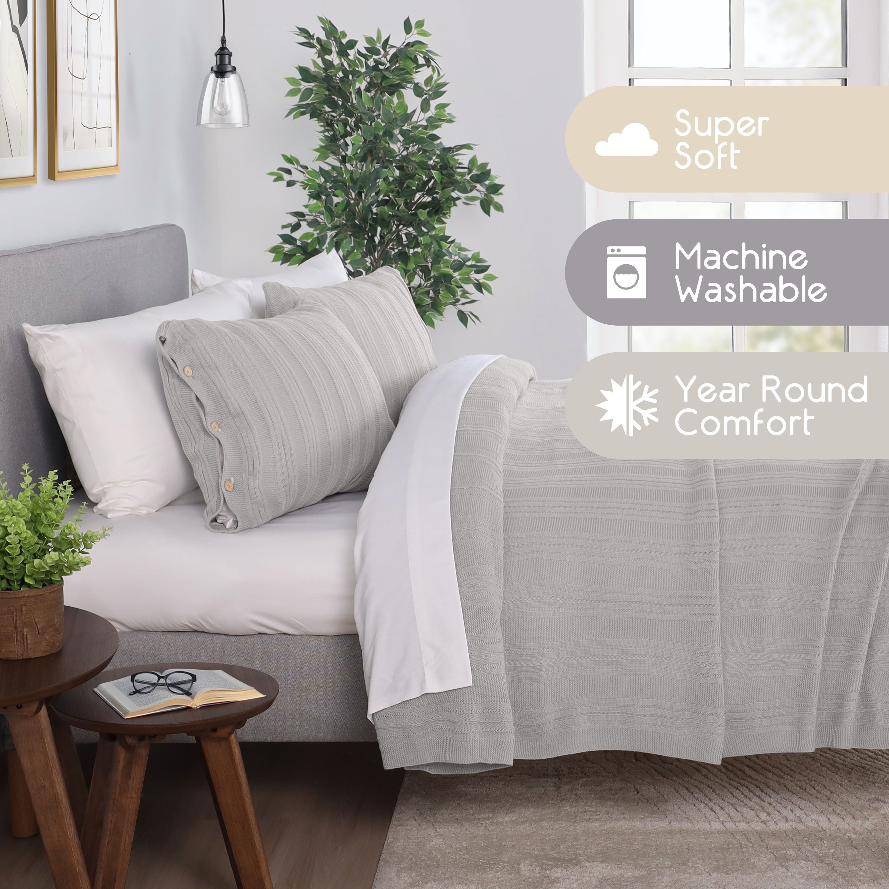 Light gray blanket set with textured design, two pillows, and a plant on a bedside table in a cozy room setting.