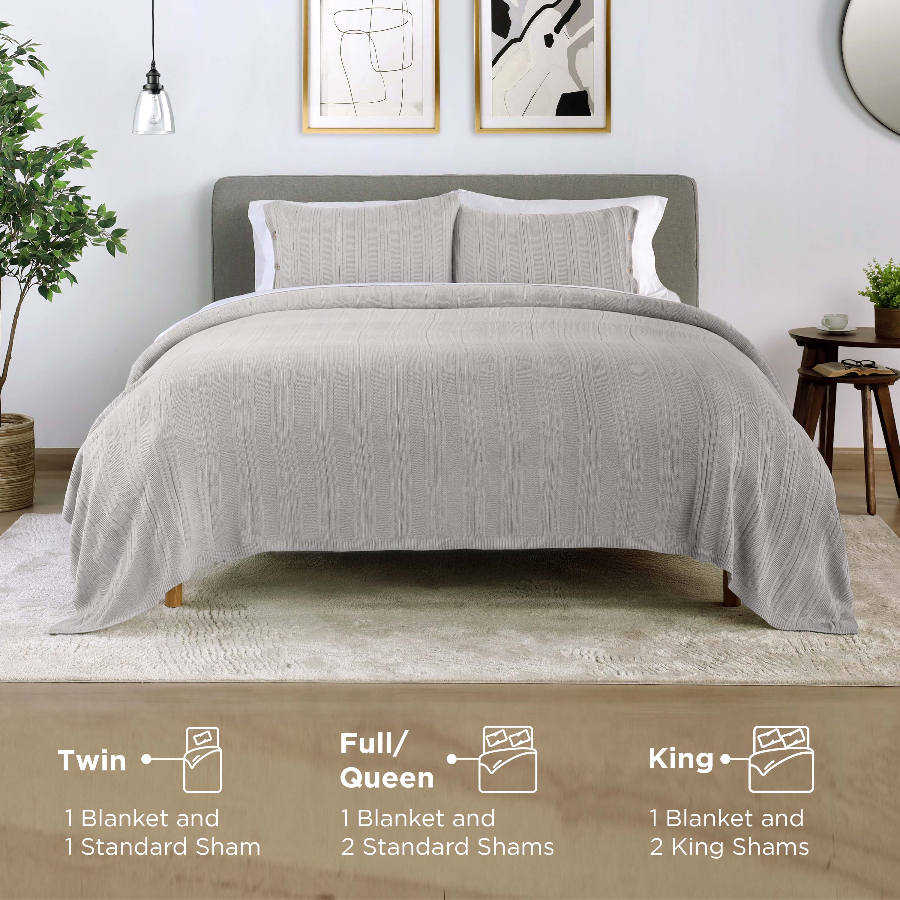 Light gray blanket set displayed on a bed with two shams, accompanied by a side table and decorative elements.