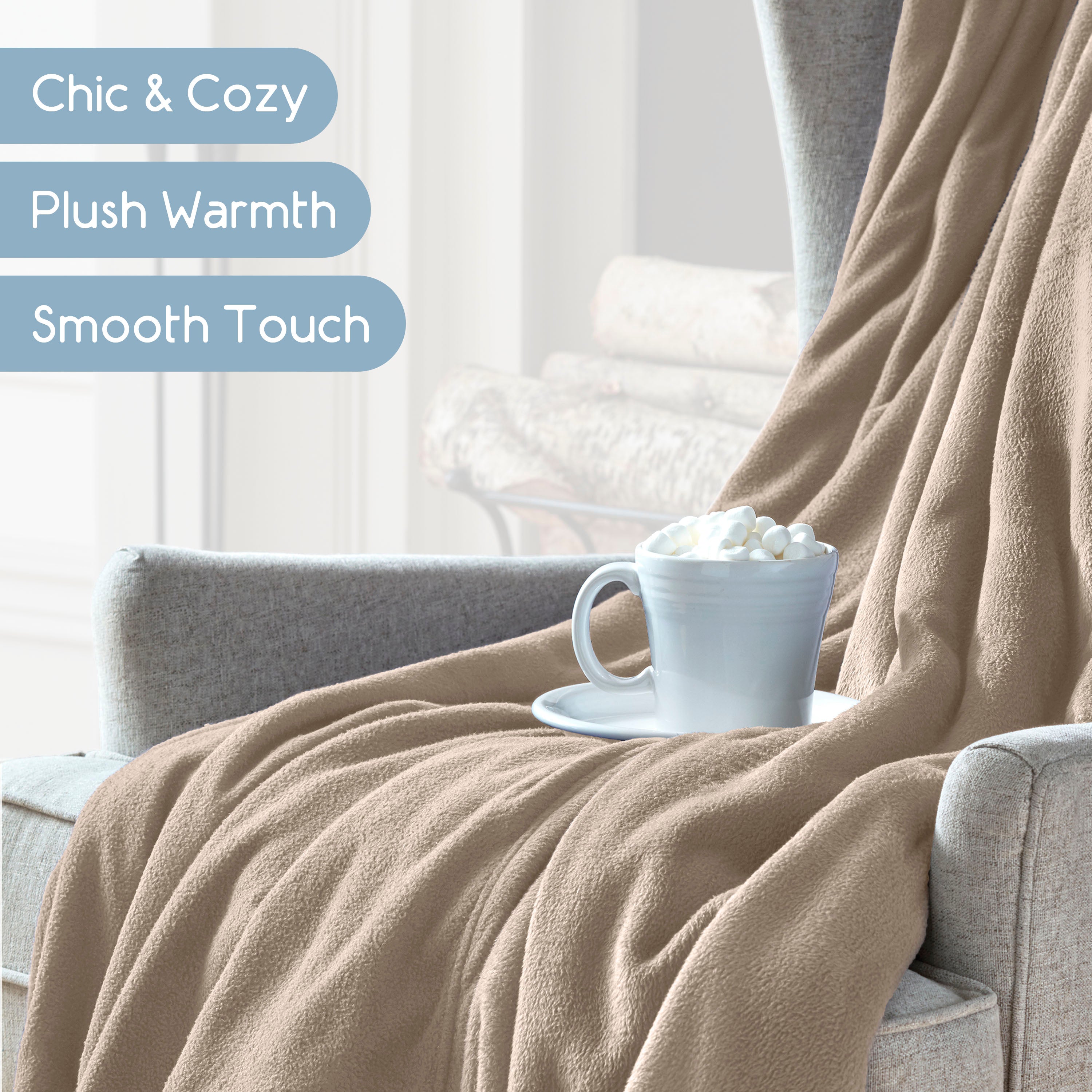 A beige microfleece blanket drapes over a gray armchair, with a cup of hot chocolate topped with marshmallows on a saucer.