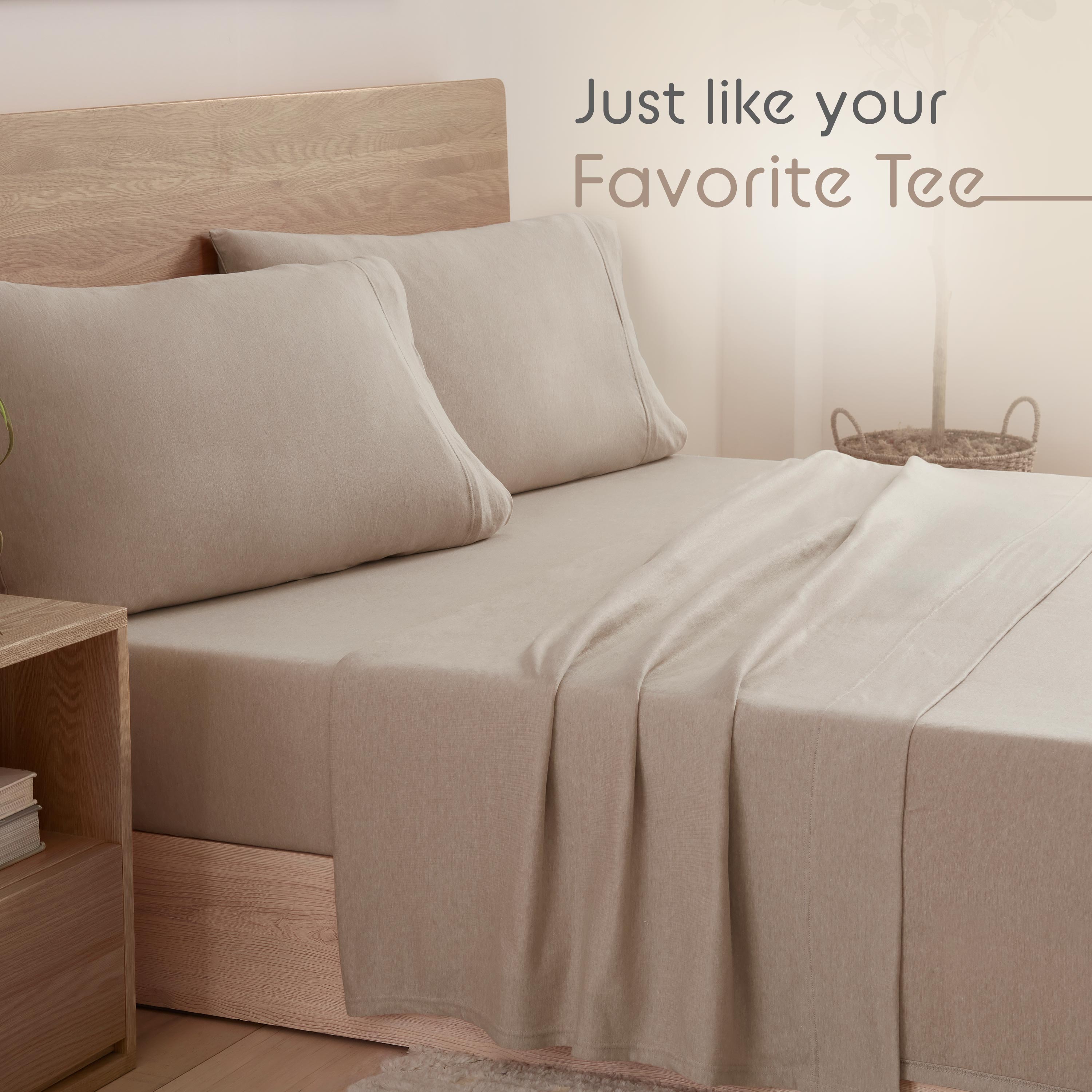 Beige bed with two large pillows and a soft sheet draped over the mattress, next to a wooden nightstand.