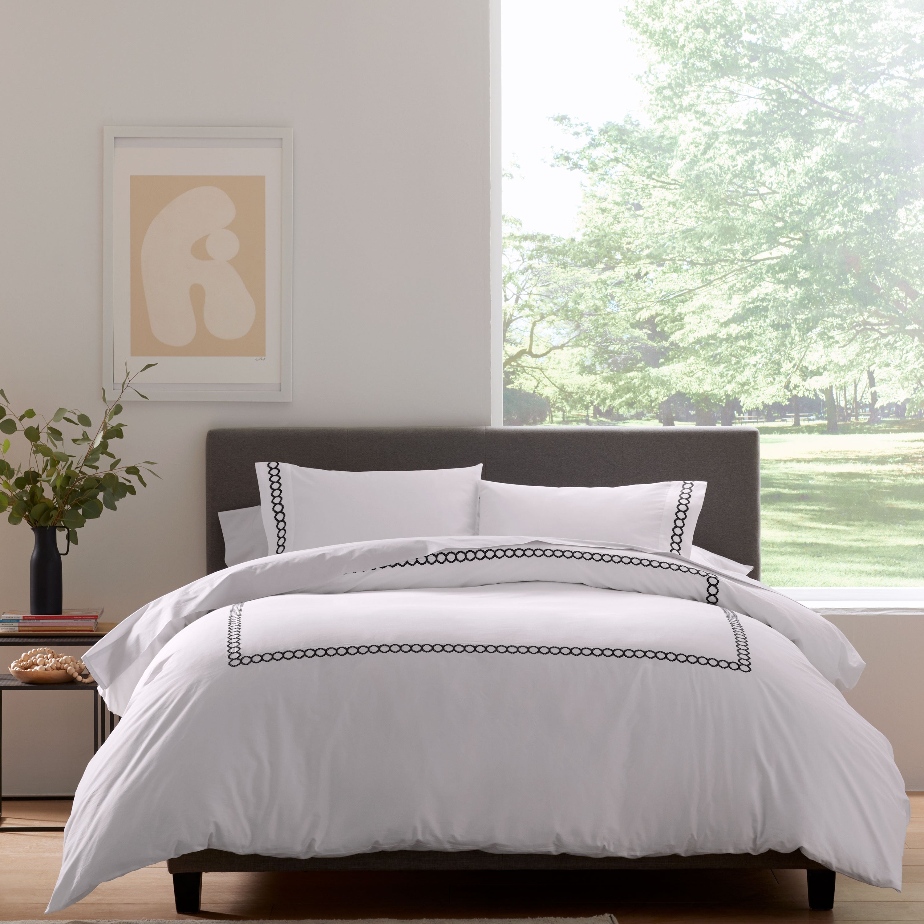 White comforter set with black trim, paired with matching pillow shams, on a bed against a bright window view.