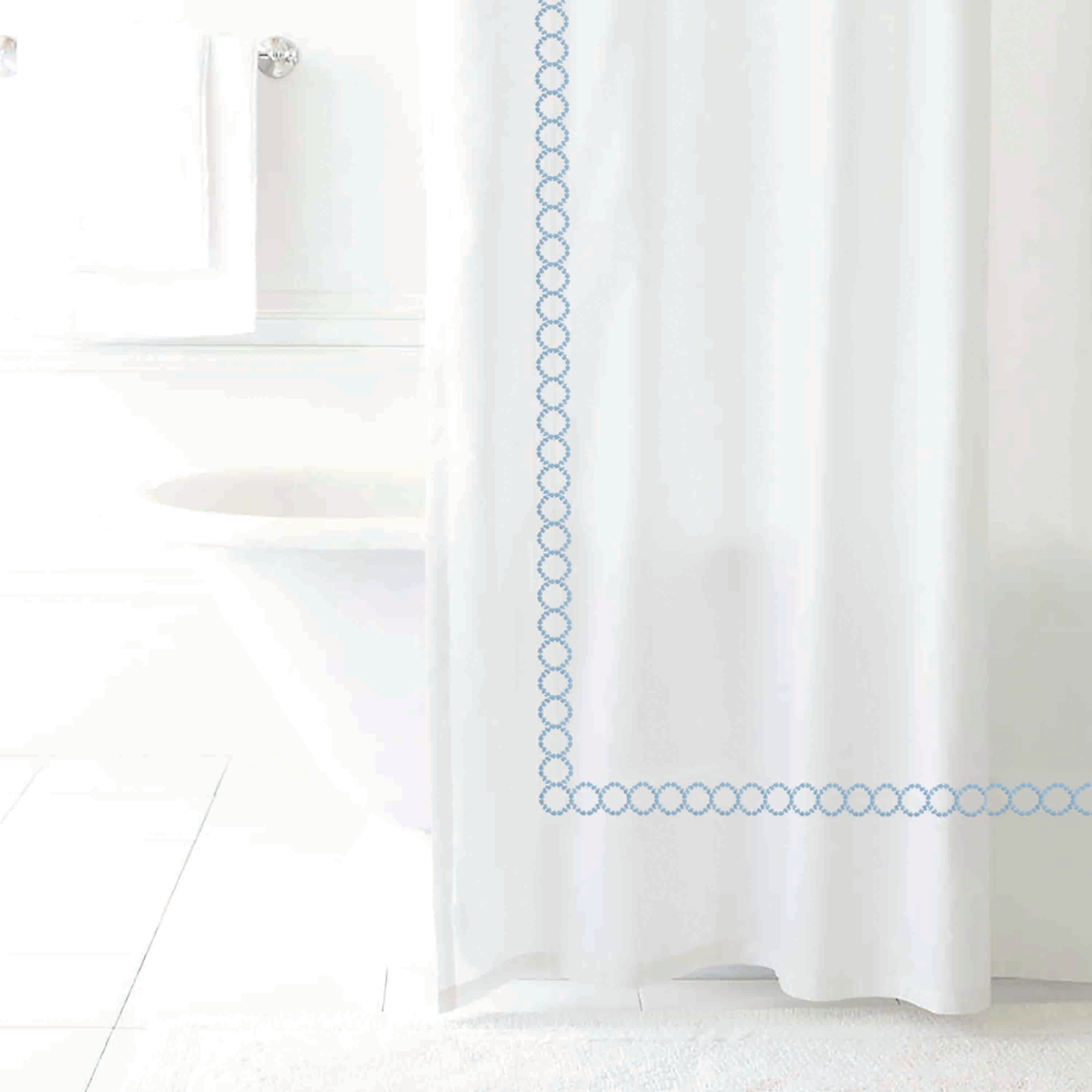 White shower curtain with a blue circular pattern along the edge, set in a bright bathroom environment.