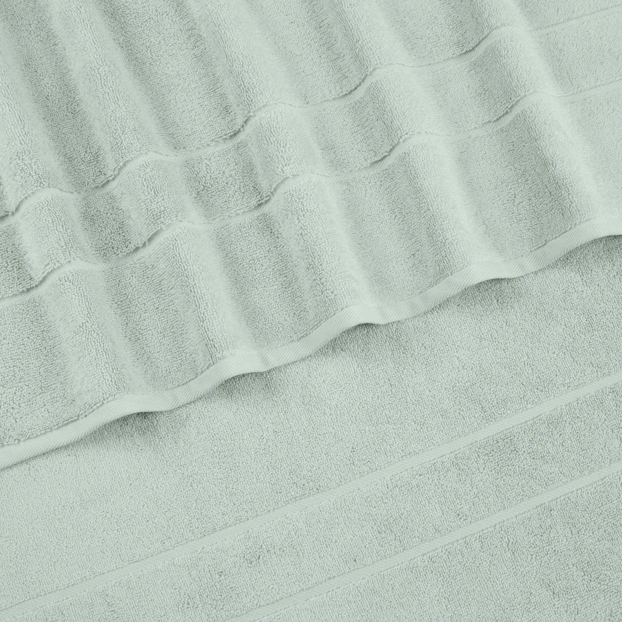 A close-up of a sage terry cloth hand towel with a textured striped pattern and folded edges.