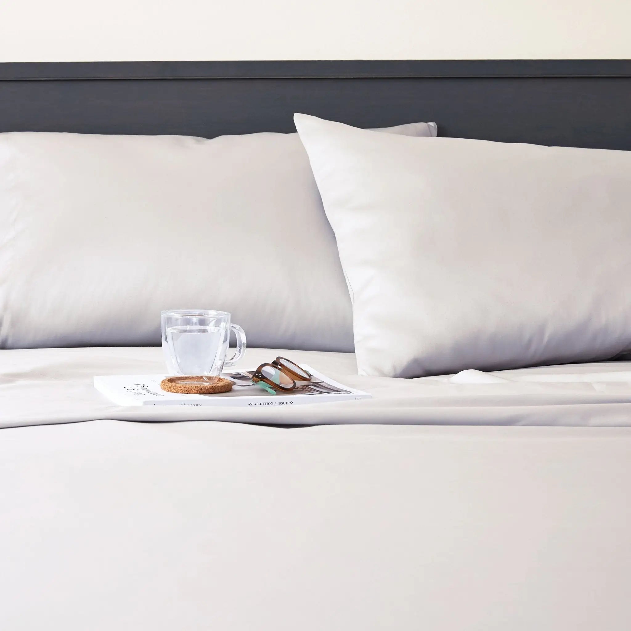 A close-up of a neatly made bed with white bedding, two white pillows, a dark headboard.
