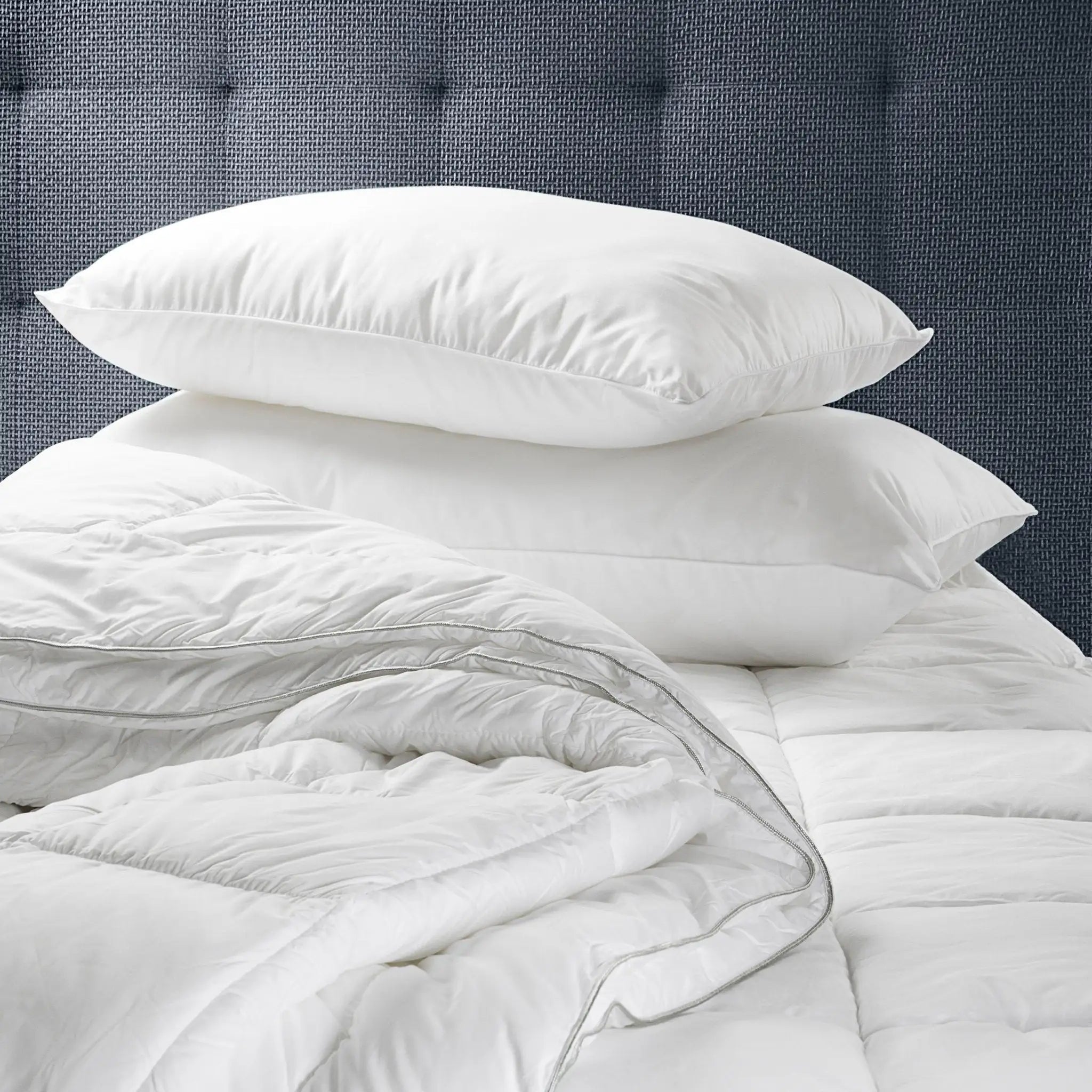 Stack of white pillows and comforter on a bed with a gray headboard.
