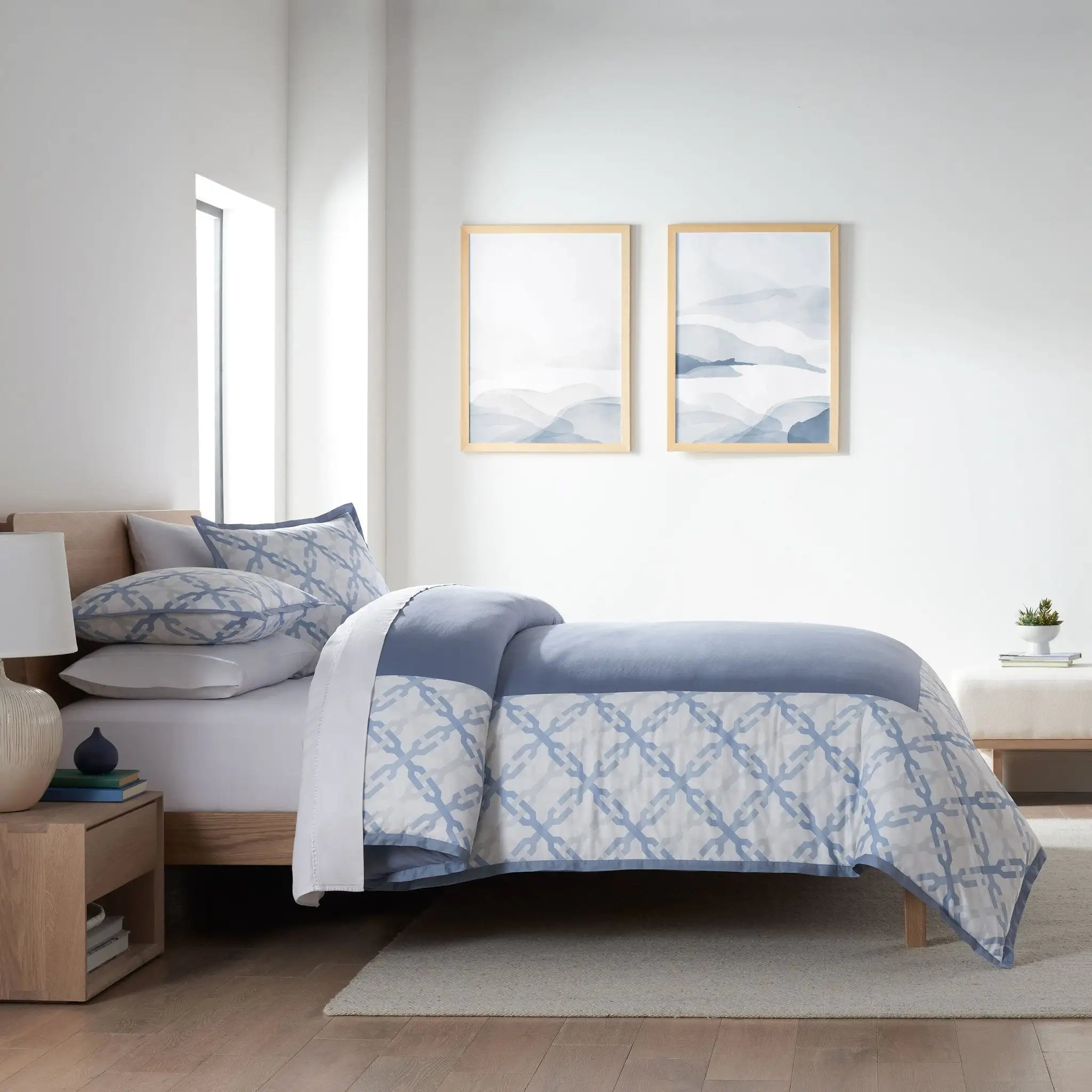 Bedroom with a bed covered in a blue and white patterned comforter, two framed artworks on the wall, and wooden nightstands.