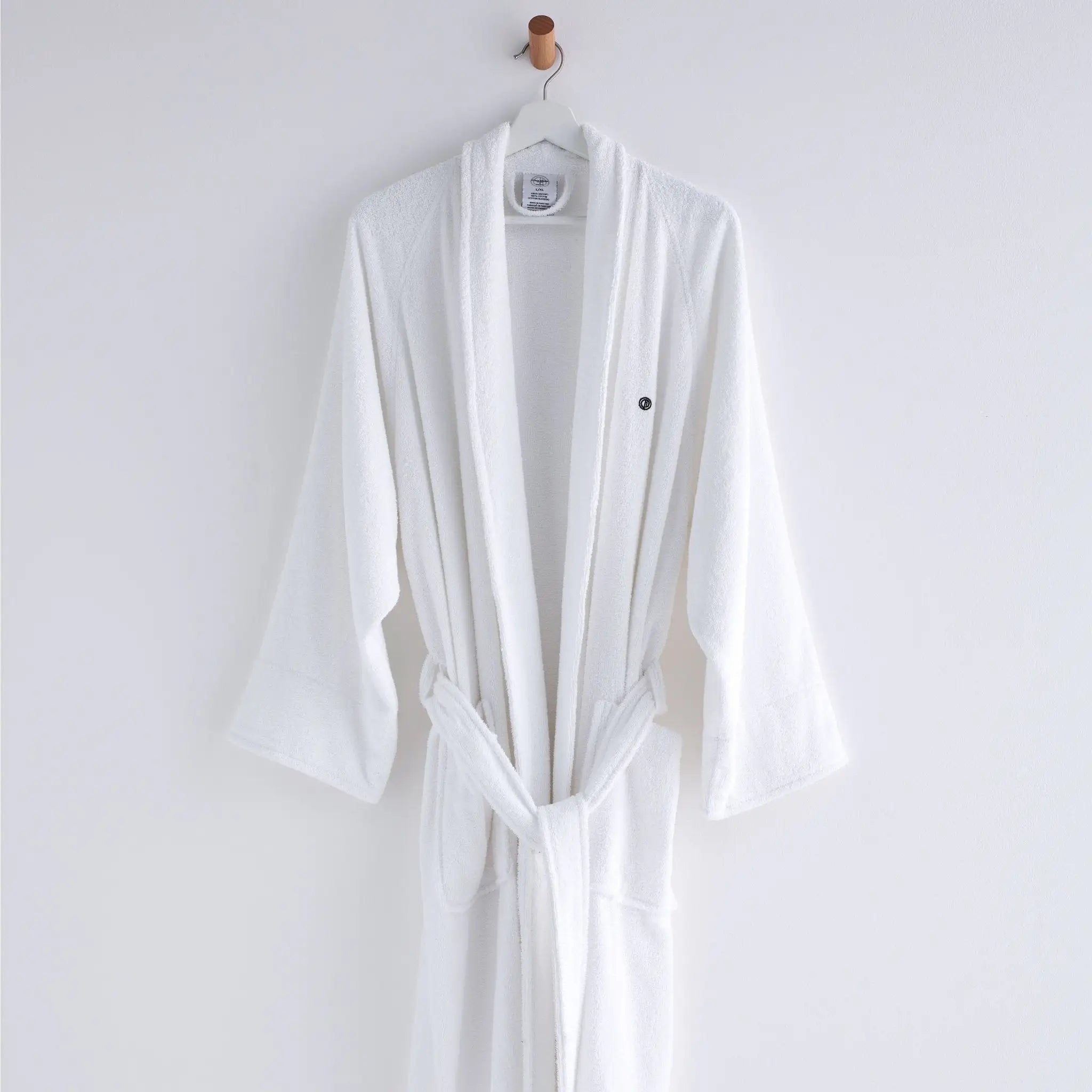 A white bathrobe hanging on a white hanger with a wooden hook against a plain white wall.