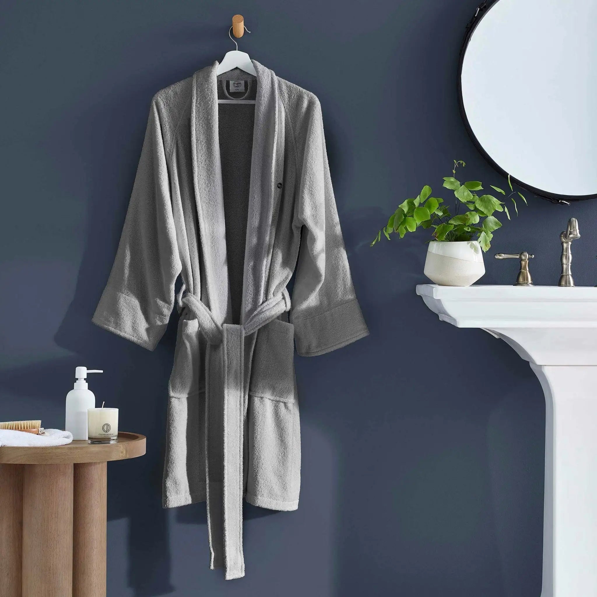 A light gray plush bathrobe hanging on a wooden hanger against a dark blue-gray wall.
