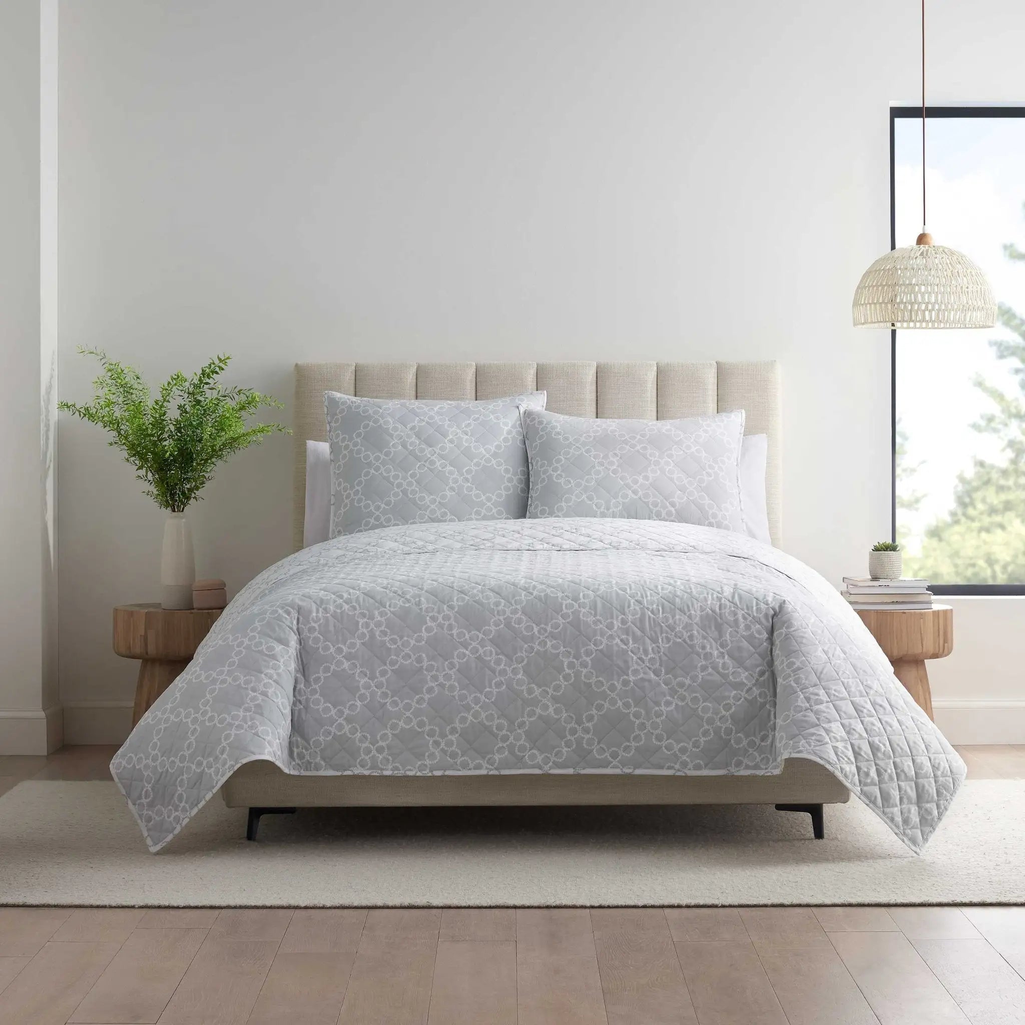 Bed with light gray patterned quilt set in a bright bedroom setting