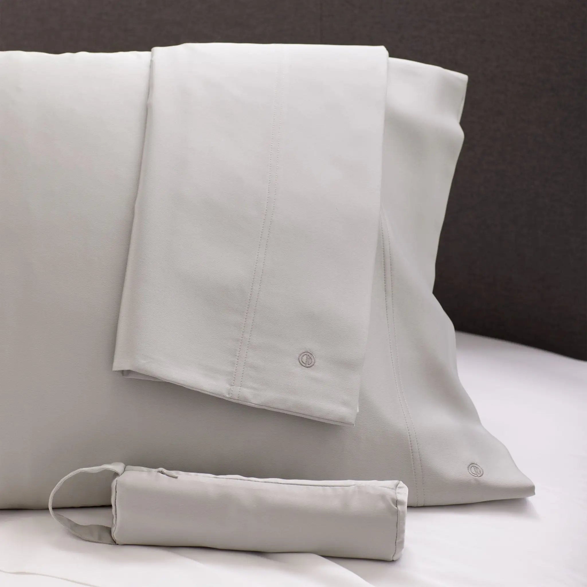 Set of light gray bedding with a matching travel bag on a bed.