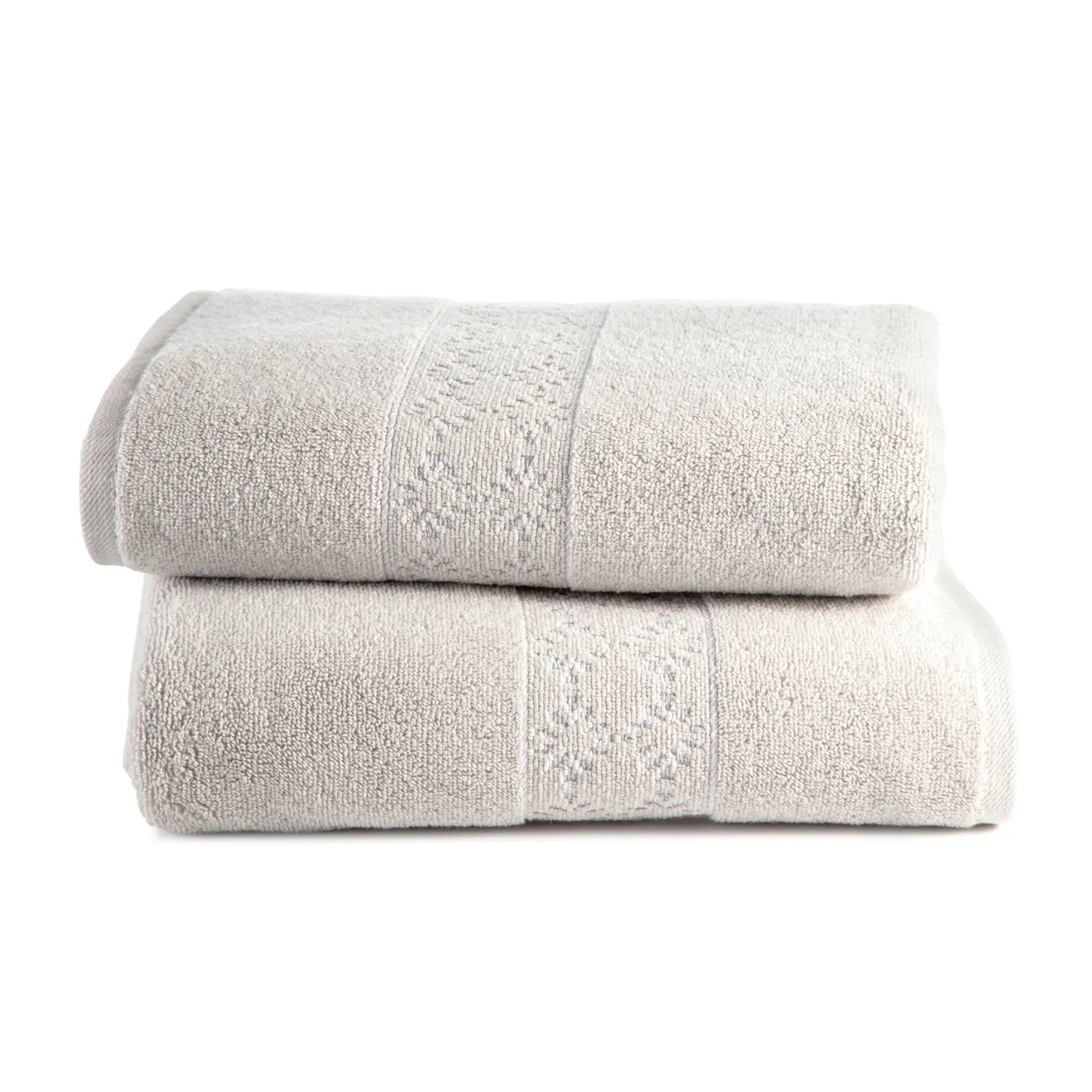 Two folded grey bath towels stacked on a white background, featuring a textured terry body and a decorative embroidered border.