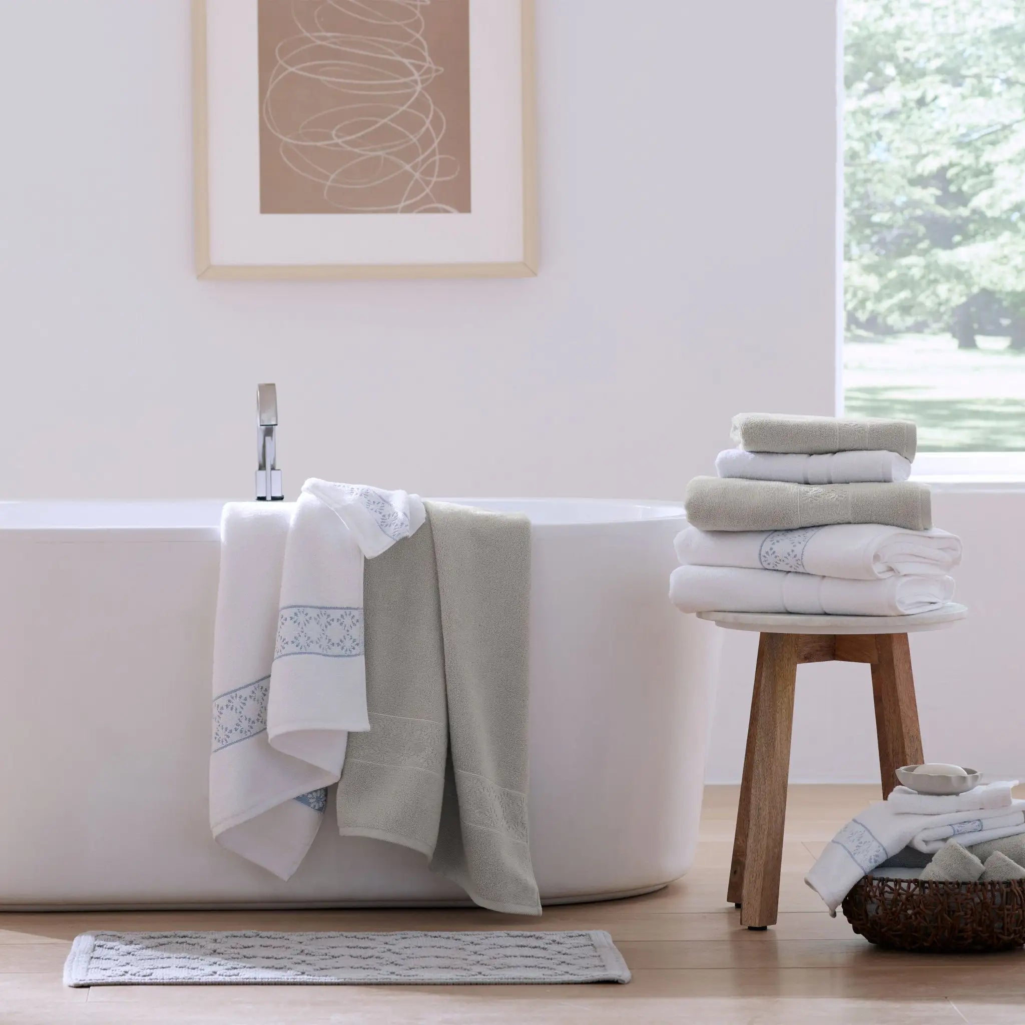 Folded and draped towels in white and light gray with blue patterned borders on a small wooden stool.