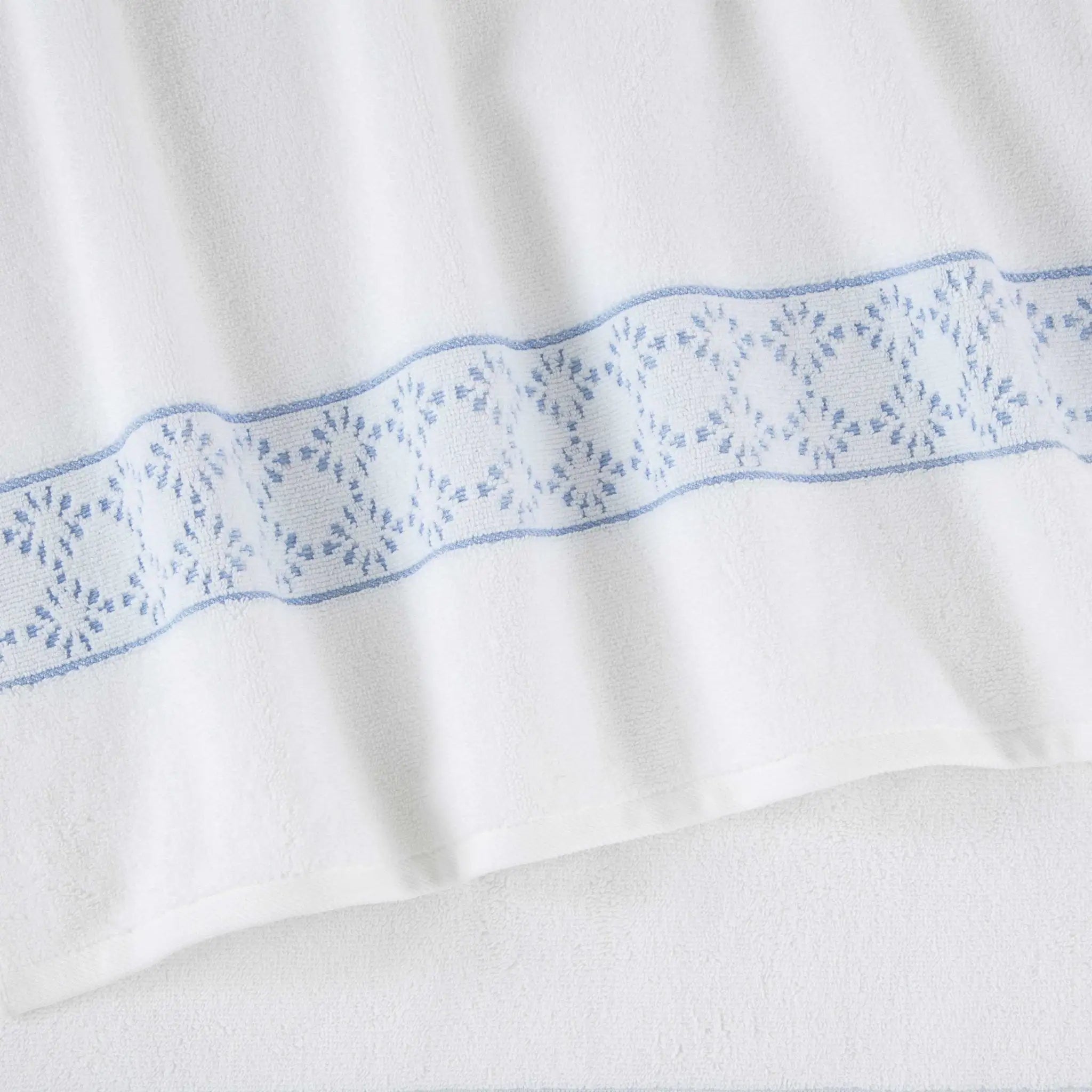 A close-up of a white fabric towel featuring a decorative horizontal band of blue embroidered geometric and floral patterns.