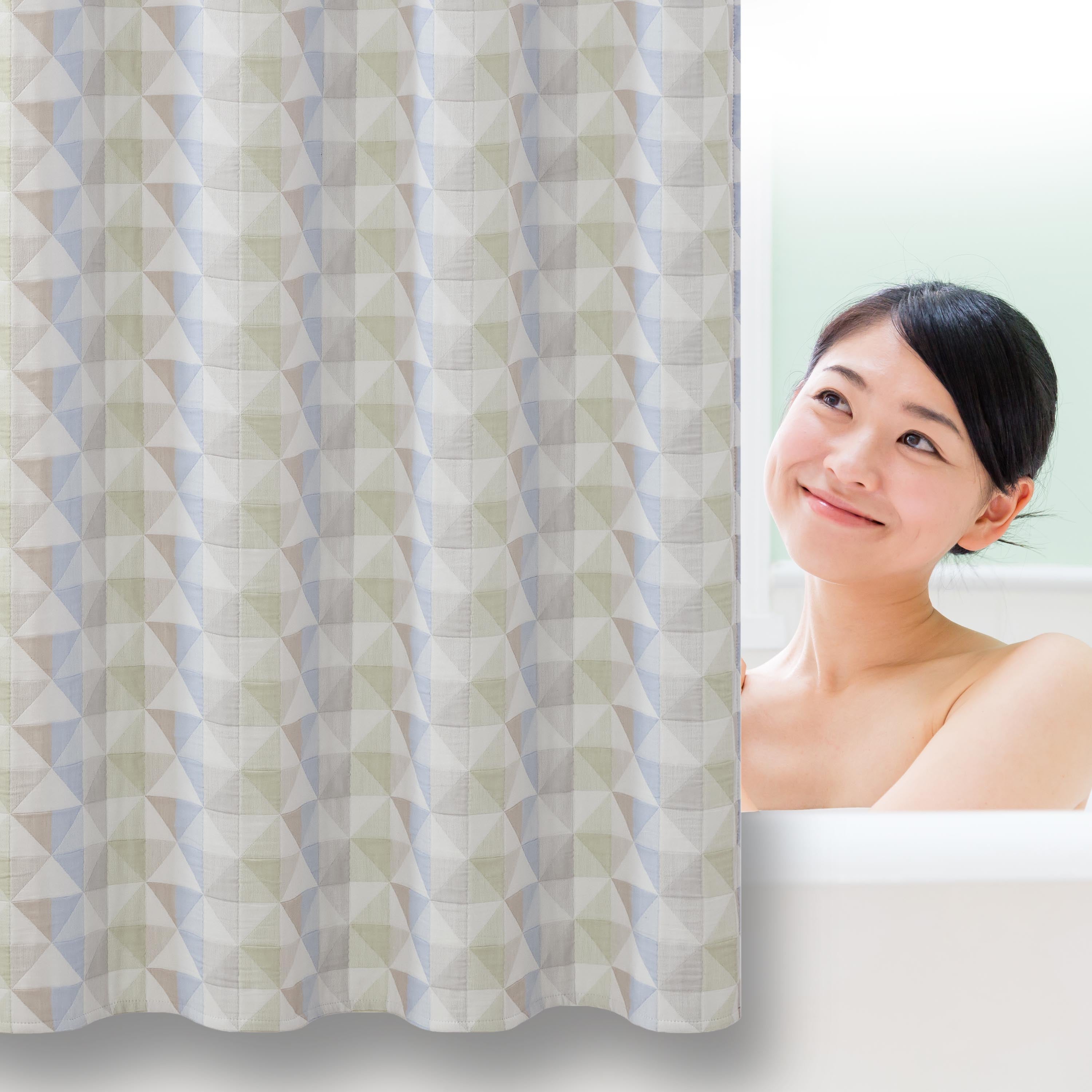 Shower curtain with a geometric pattern in soft colors, partially obscured by a smiling person in a bathtub.