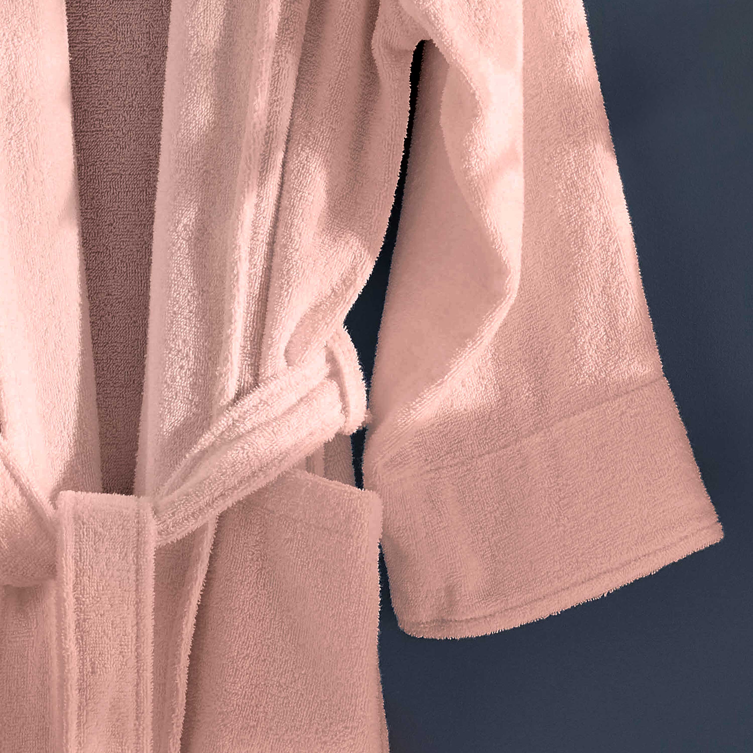 Light pink terry bath robe with a belt and wide sleeves hanging against a dark background.