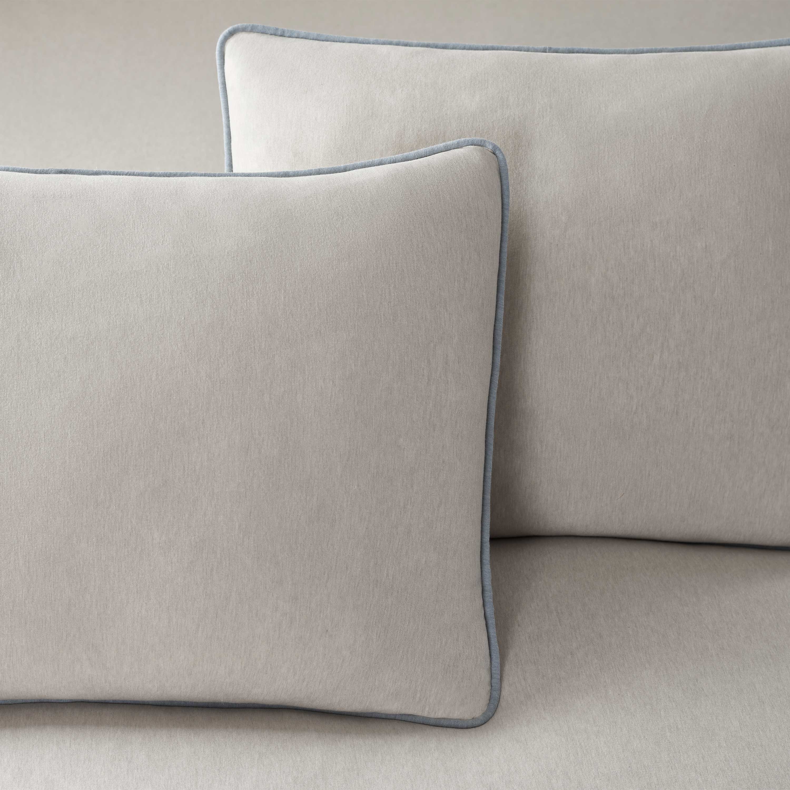 Two light gray pillows with a subtle blue trim, resting on a matching fabric surface.