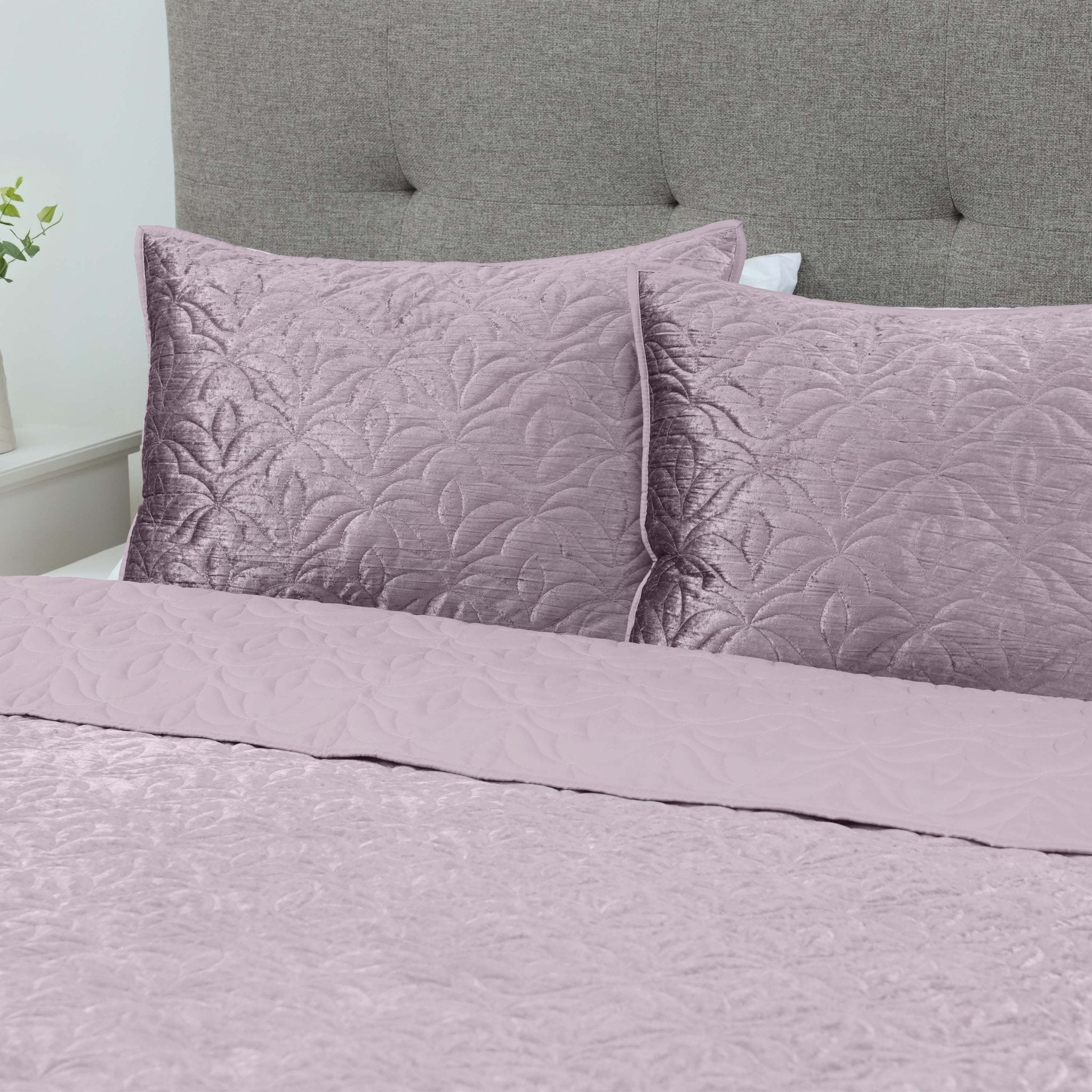 Purple quilt set on a bed with a gray upholstered headboard.