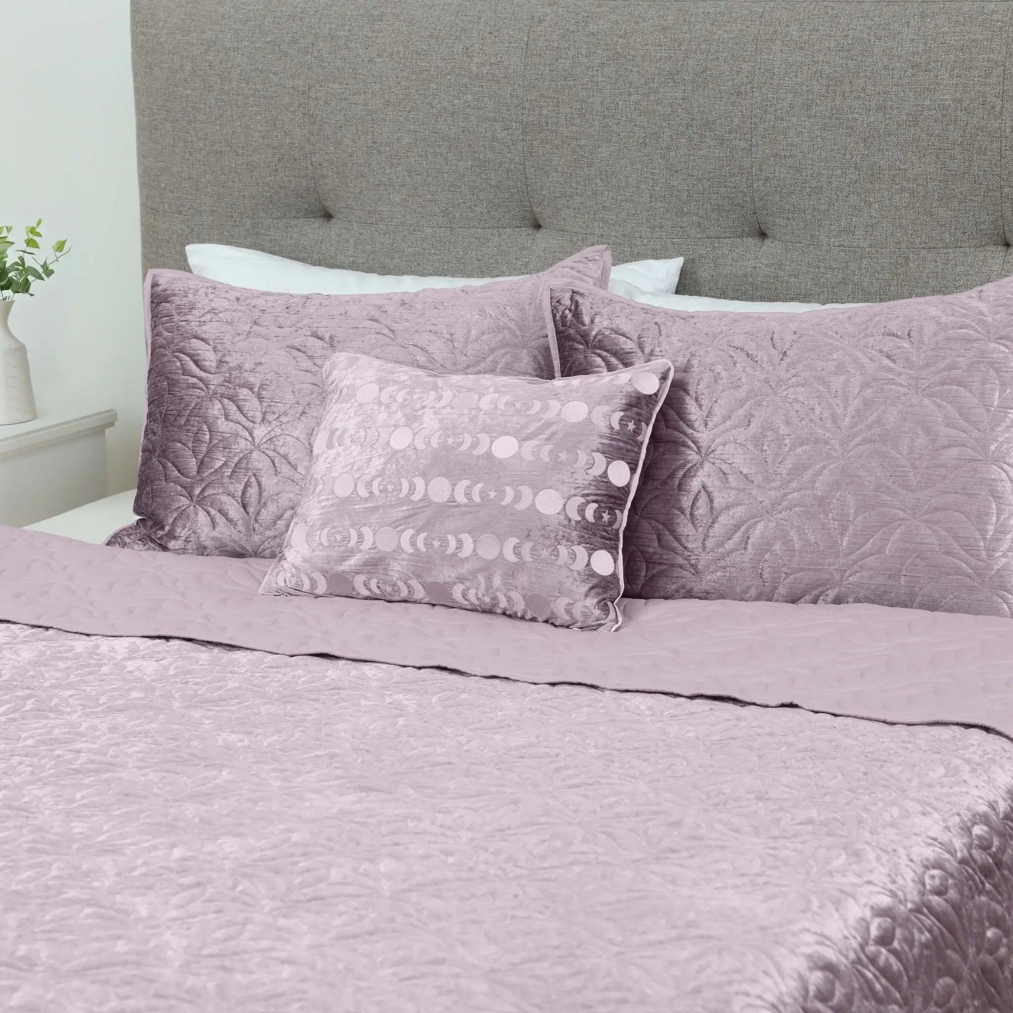 A bed dressed in a dusty lavender bedding set with textured floral-patterned pillows and a matching quilt.