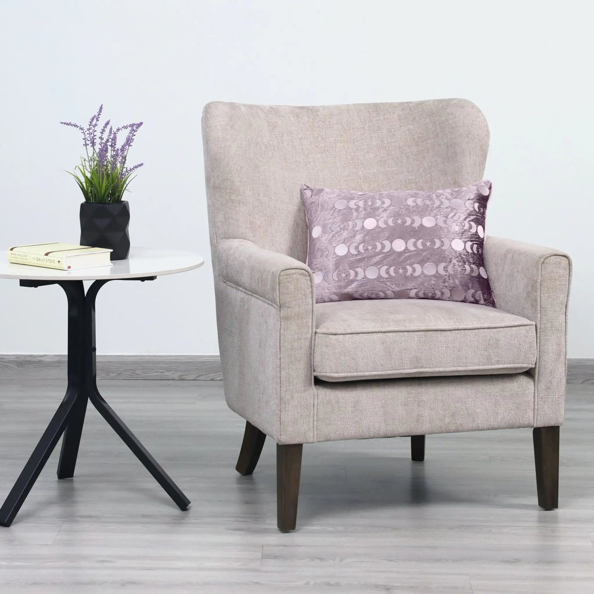 A light beige upholstered armchair with a patterned purple throw pillow.