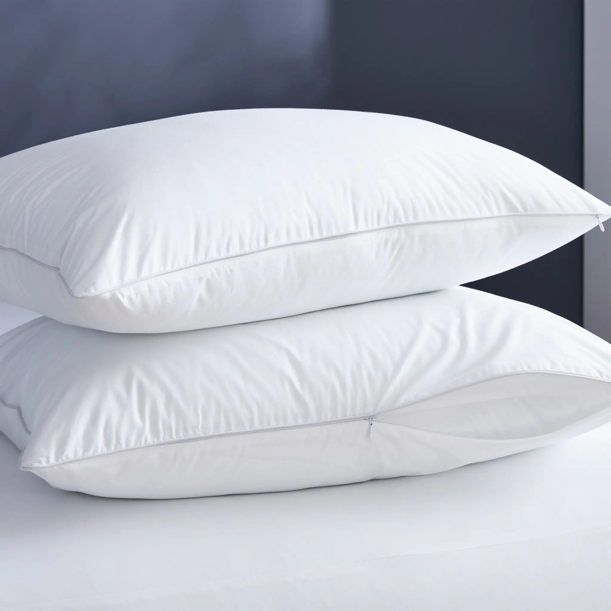 Two white fluffy pillows stacked on a white bed against a dark gray headboard.