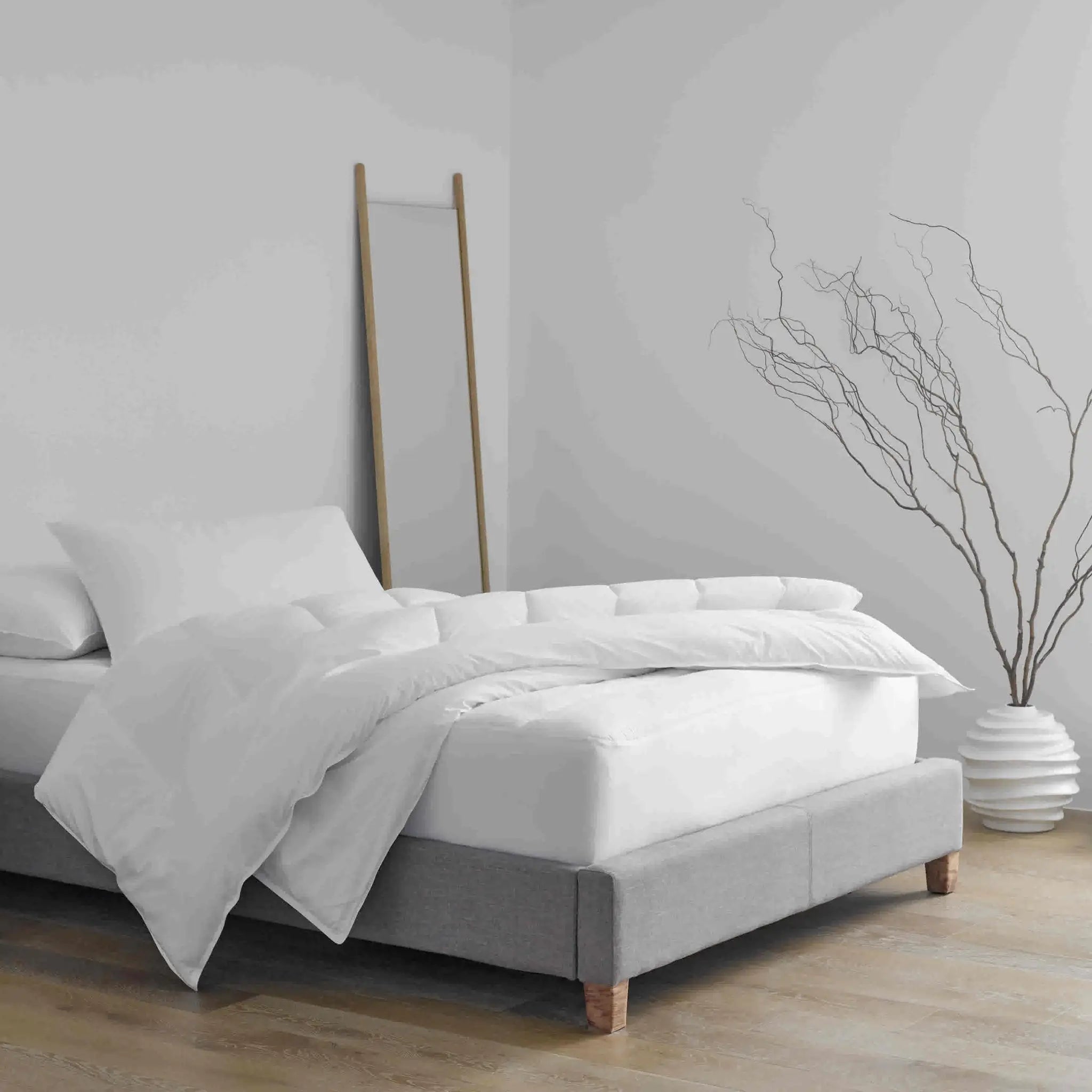 A modern bed frame with a light gray upholstered base and set in a minimalist bedroom.