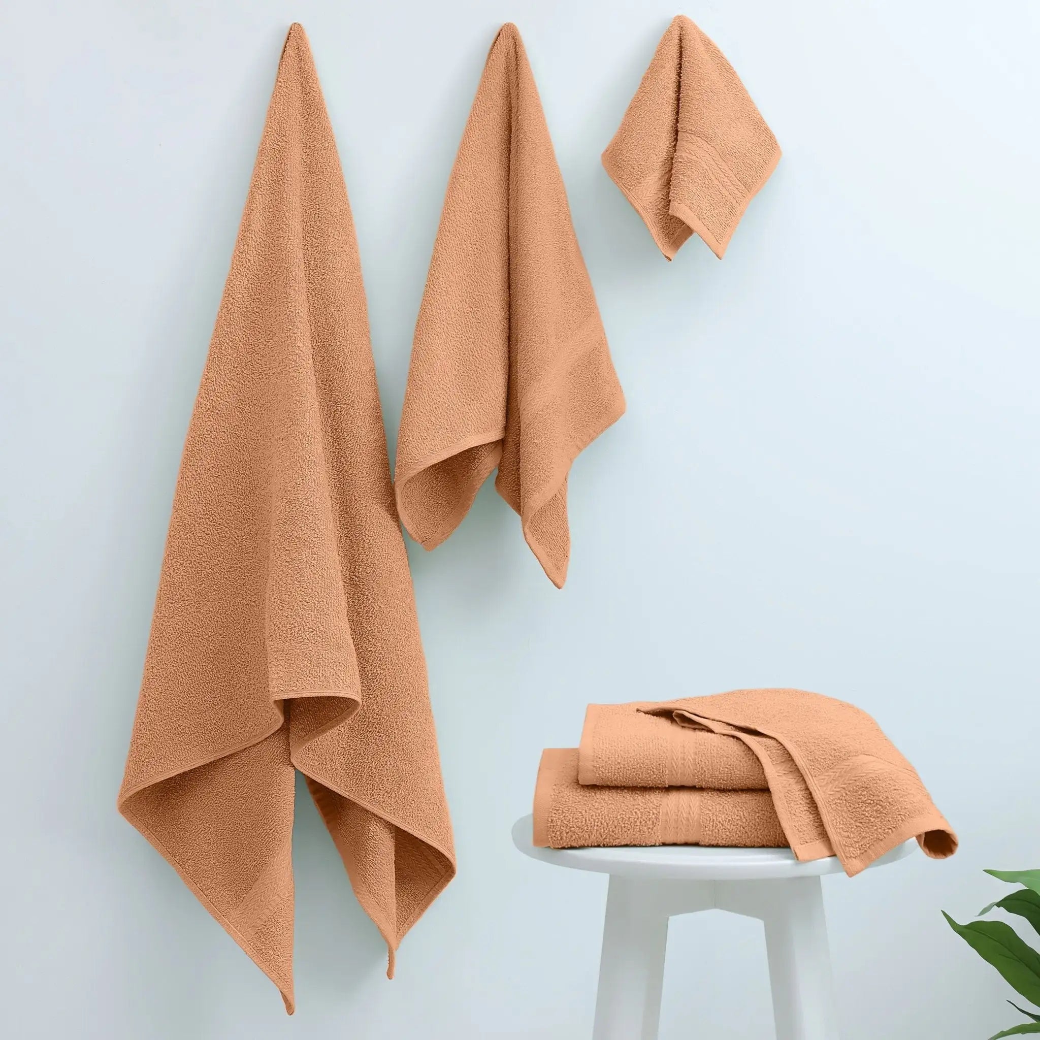Three peach-colored cotton towels hanging on a light blue wall.