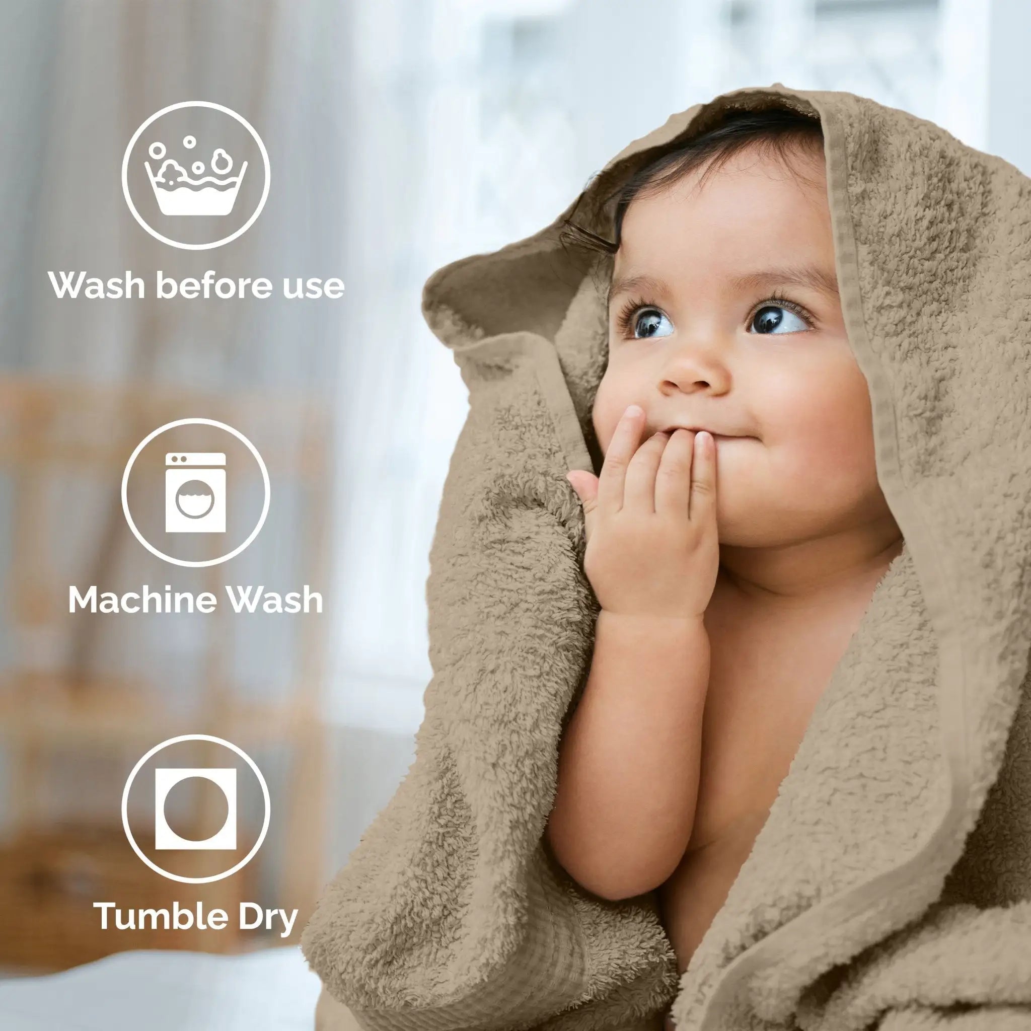 A baby wrapped in a soft beige towel, with three white circular icons and text on the left reading 'Wash before use,' 'Machine Wash,' and 'Tumble Dry.' The background is a softly blurred indoor setting.