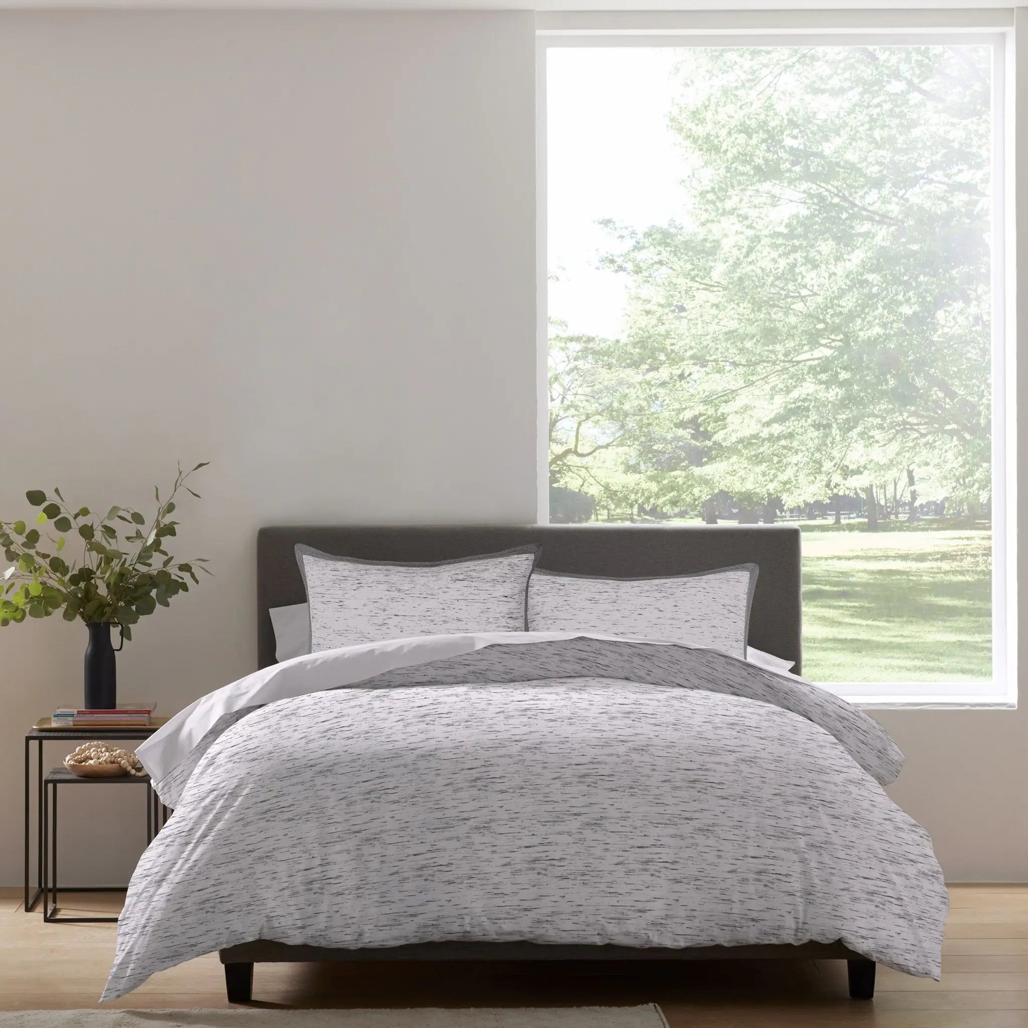 A bed dressed in a light gray and white patterned comforter set.