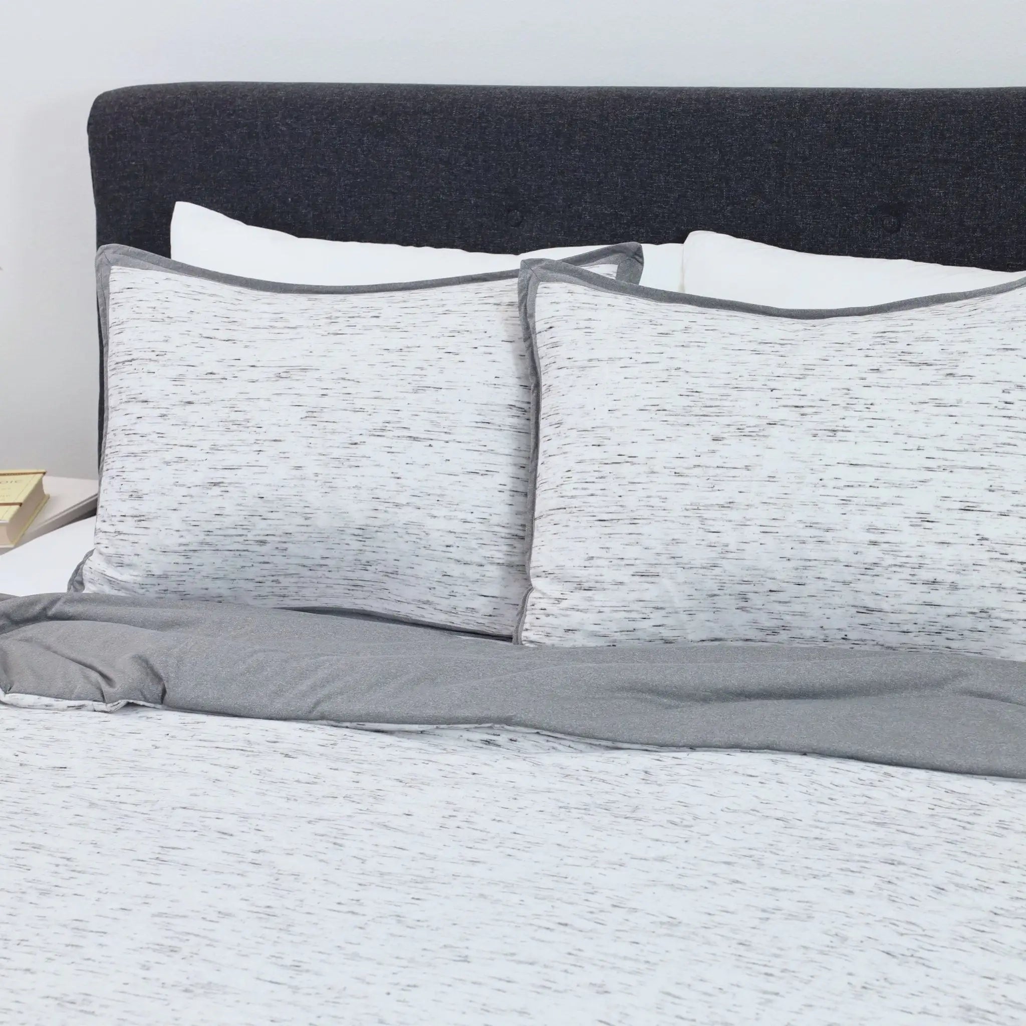 Gray and white comforter set on a bed with a dark gray headboard.