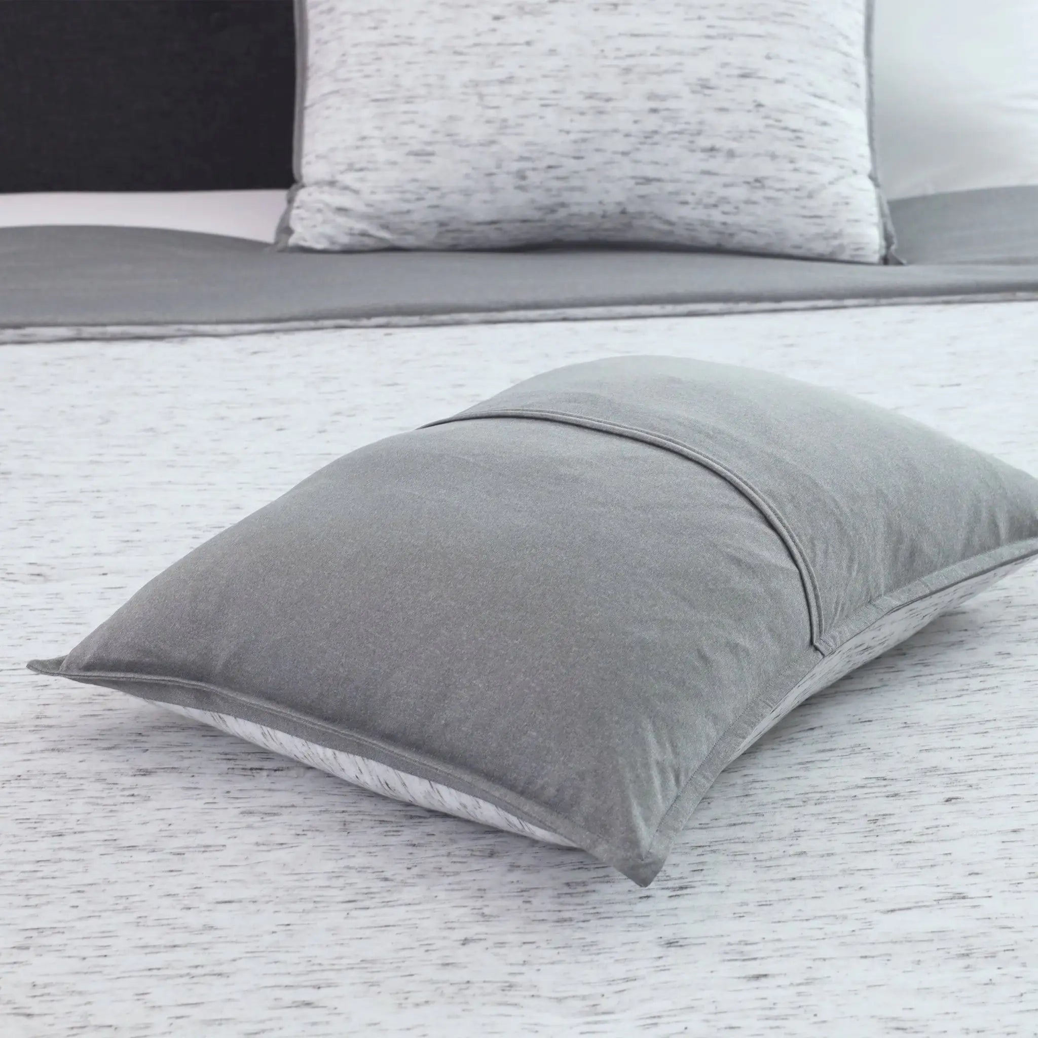 Gray pillow sham on a bed with a white and gray patterned pillow sham in the background.