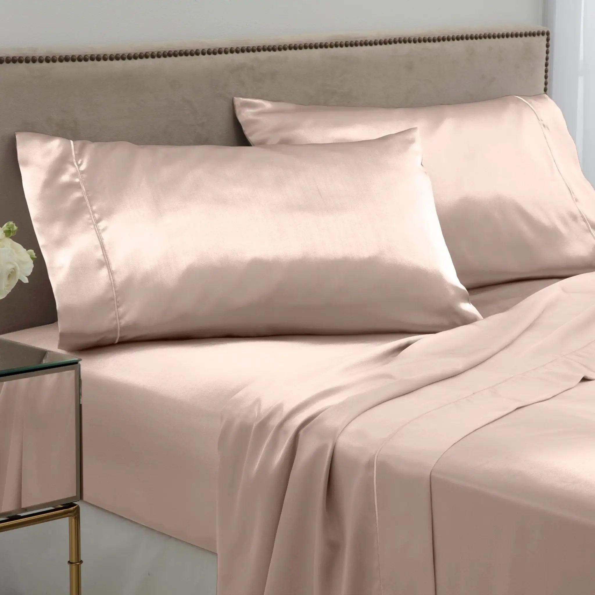 Pink bed sheets and pillows on a bed with a neutral headboard.