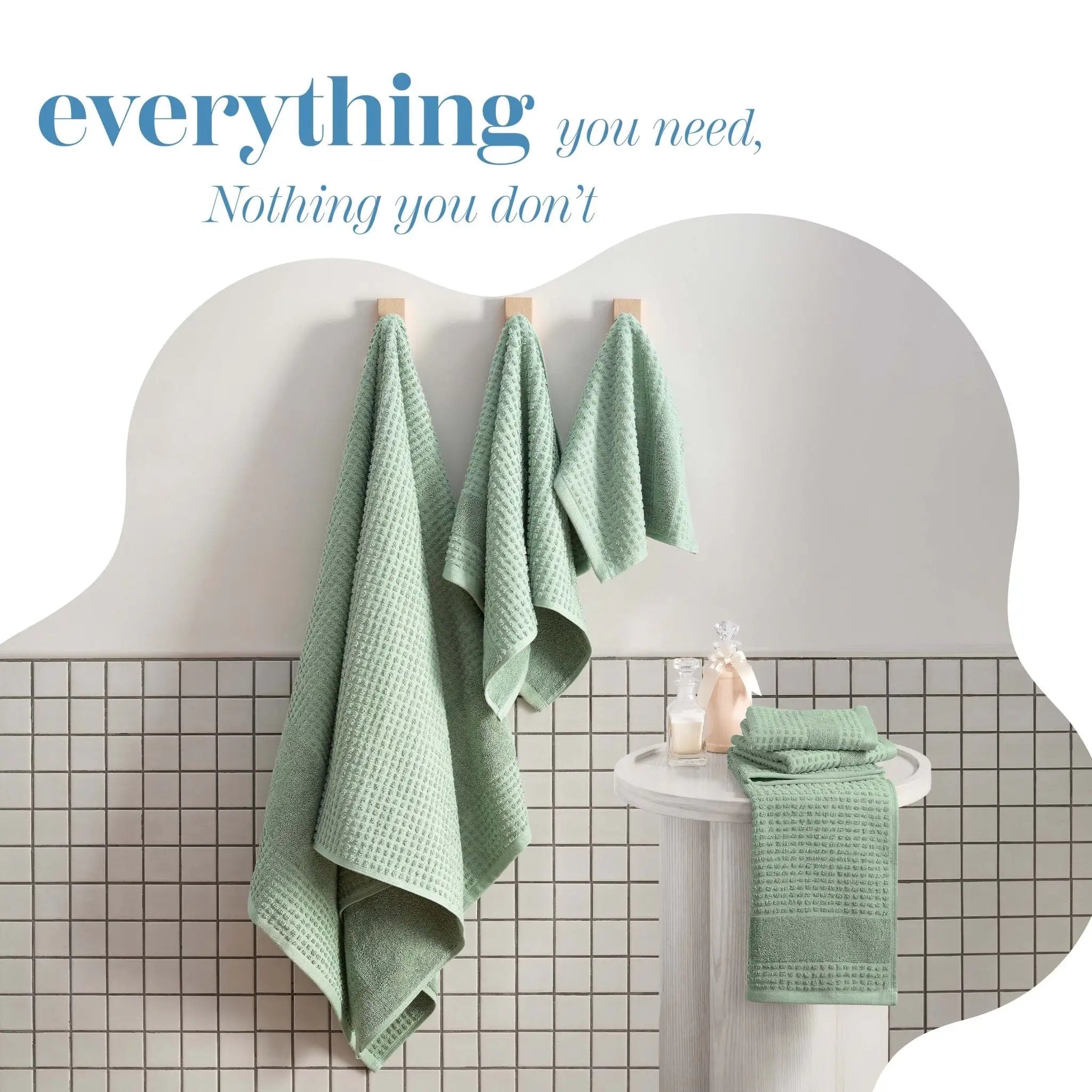 Sage towels hanging on a white towel rack against a tiled bathroom wall.
