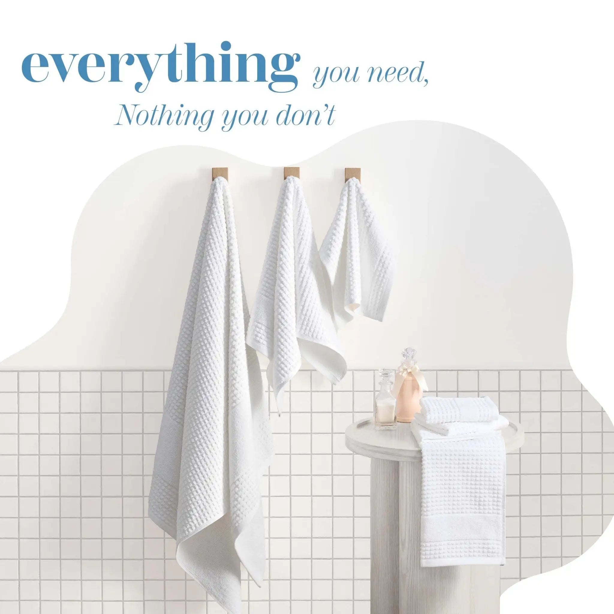 Three white towels hang from wooden hooks on a wall. Decorative text at the top reading 'everything you need, Nothing you don't'.